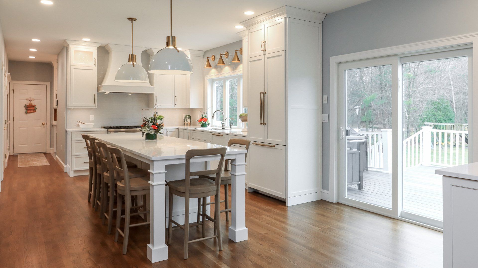 Bright modern kitchen with island, pendant lights, hardwood floors, and sliding glass doors to a deck.