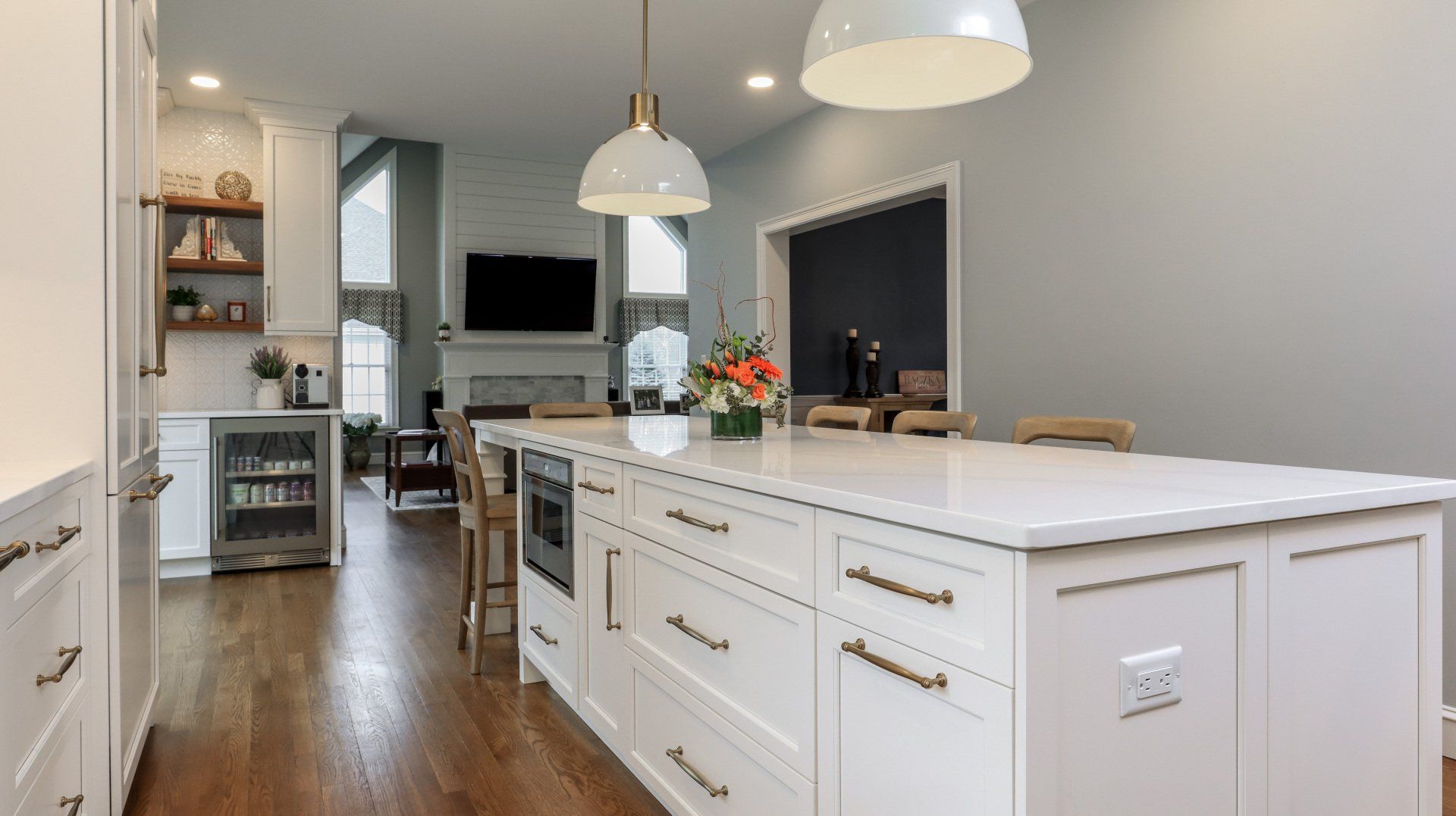 Bright white kitchen with large island, pendant lights, dark wood floors, and stainless appliances.