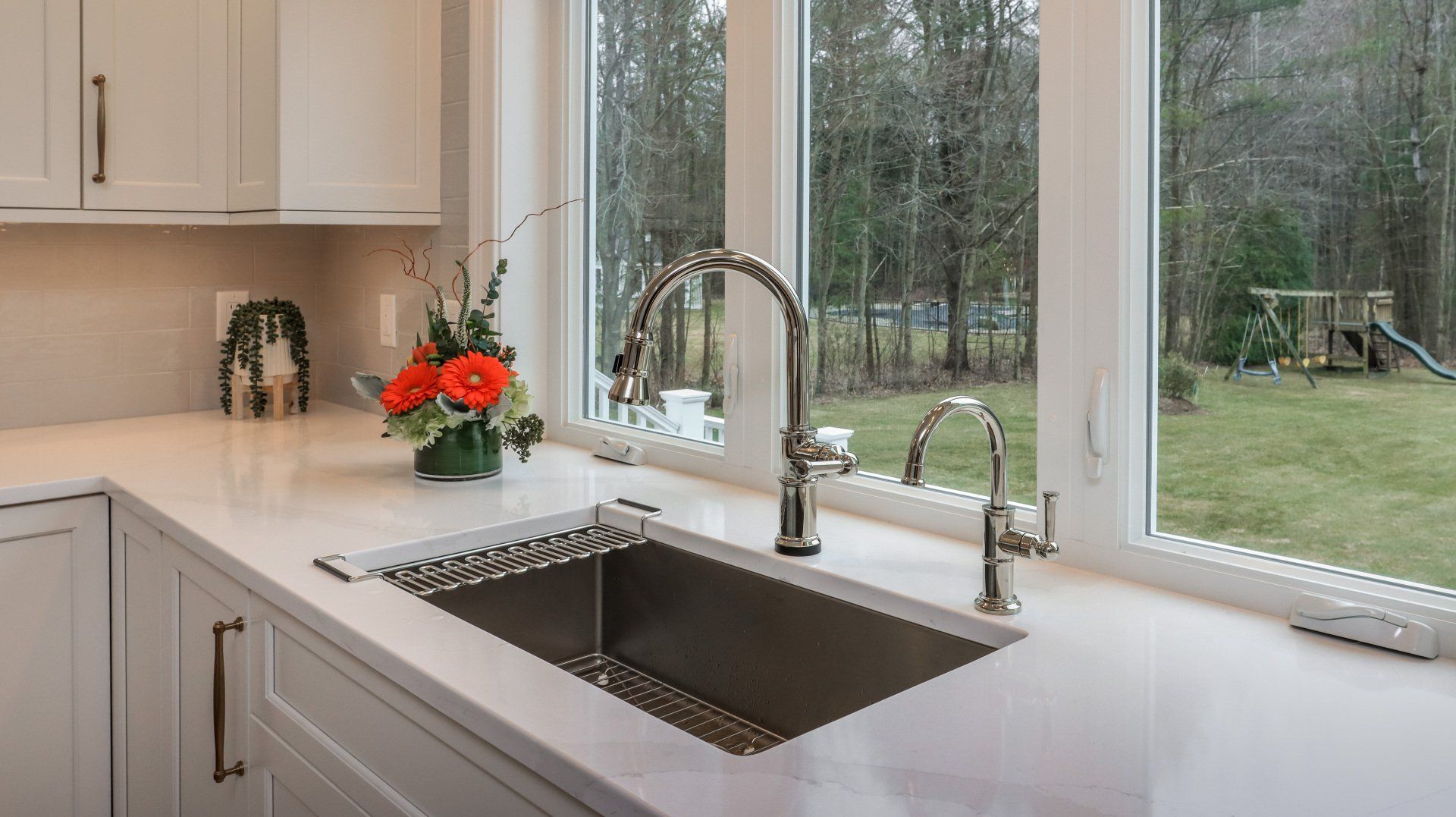 Modern kitchen sink by large windows with a chrome faucet and a vase of orange flowers