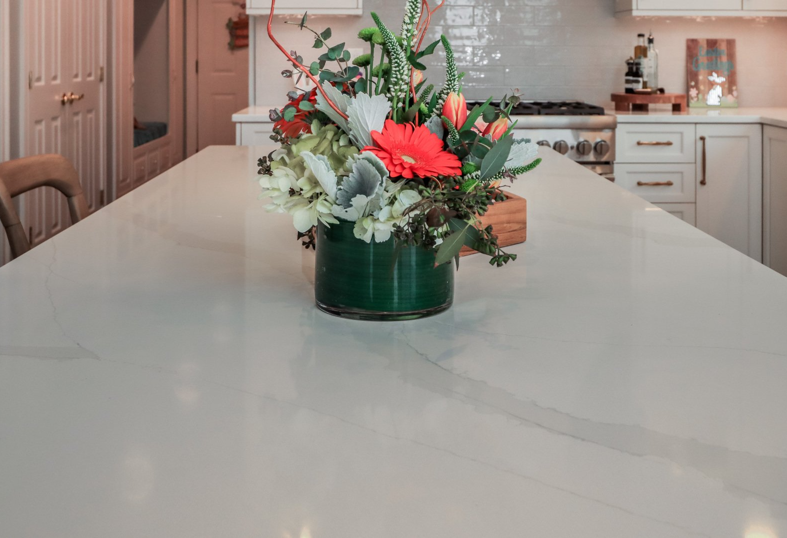 Floral arrangement in a green vase on a kitchen island, with red and white flowers.