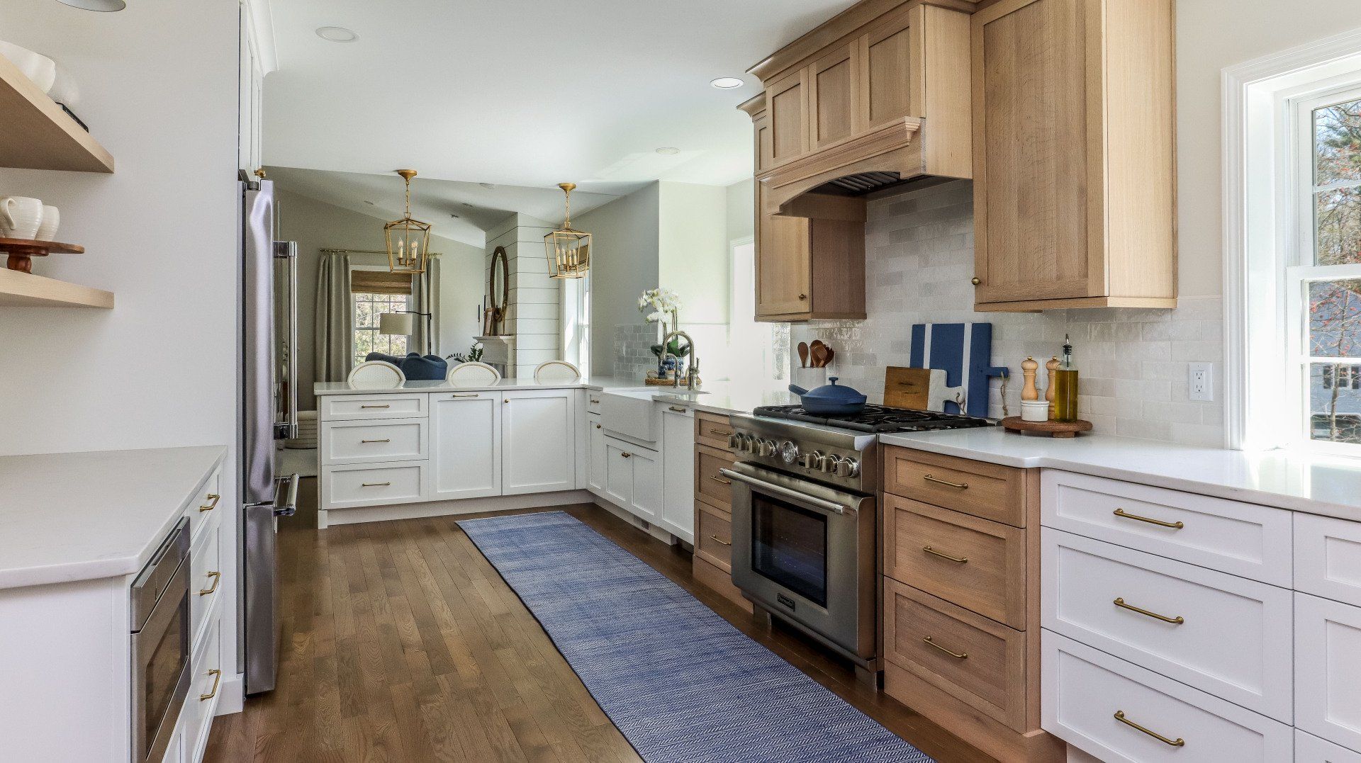 Bright modern kitchen with wood cabinets, white cabinets, stainless stove, blue runner, and hardwood floors