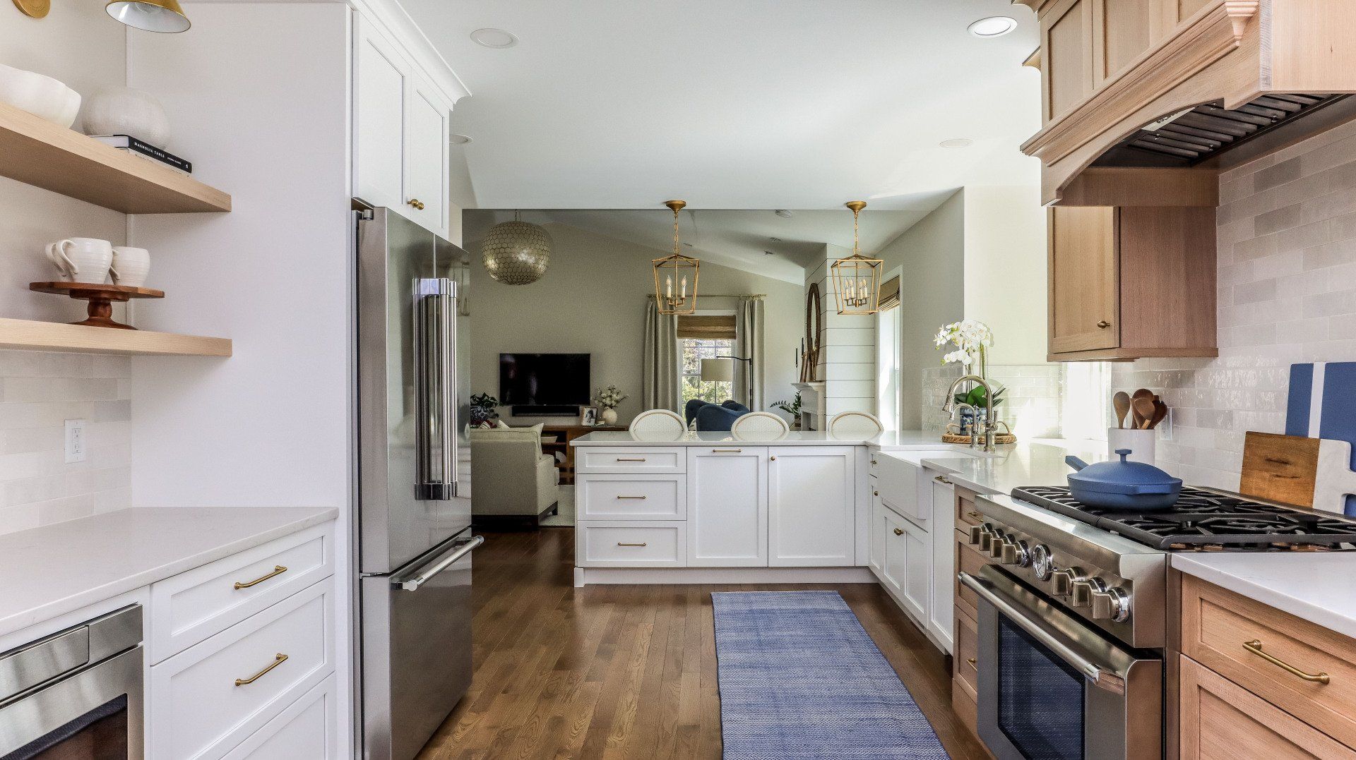 Bright modern kitchen with white cabinets, stainless steel appliances, wood floors, and a blue runner rug