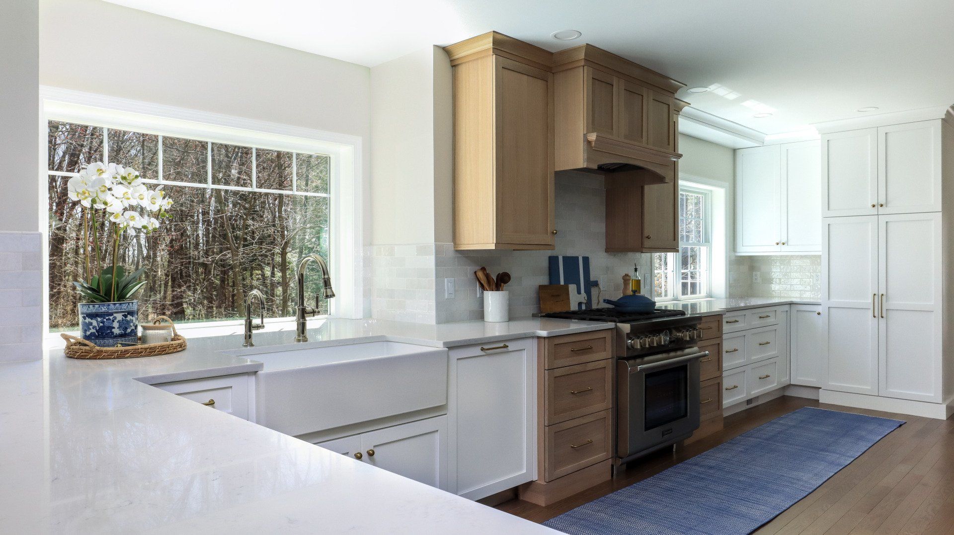 Bright modern kitchen with white counters, wood cabinets, stainless stove, and large window.