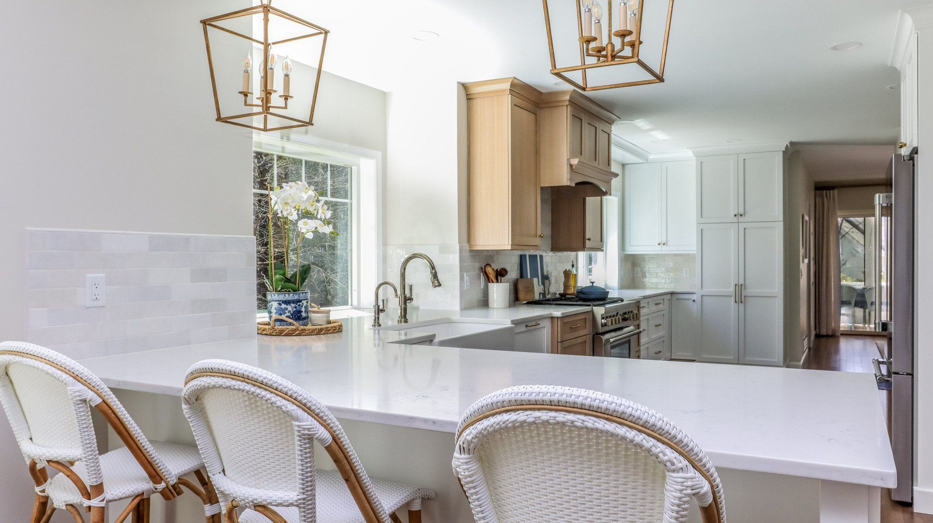 Bright kitchen with white counters, wicker barstools, gold pendant lights, and beige cabinets
