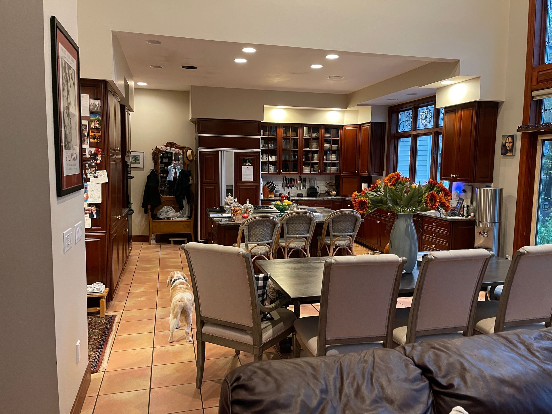 Modern dining room with glass table, upholstered chairs, tile floor, and kitchen bar in back