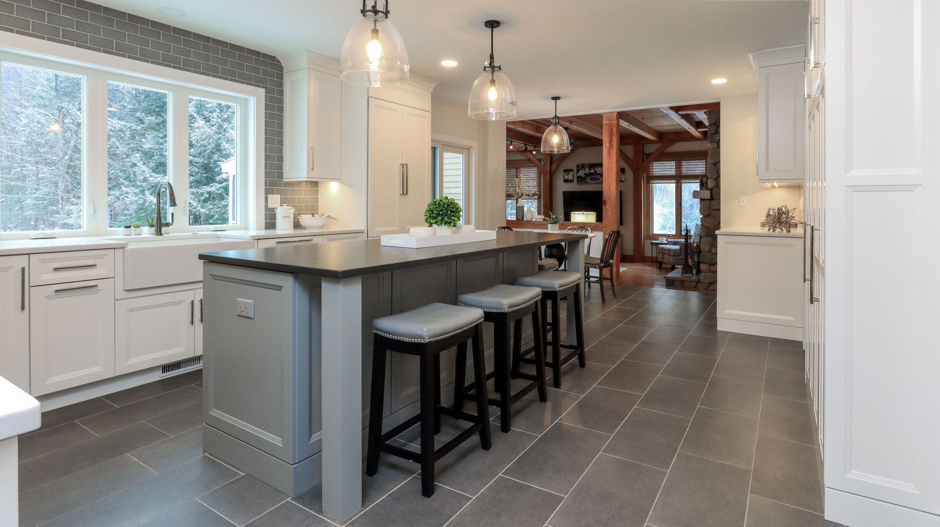 Bright modern kitchen with gray island, bar stools, white cabinets, and large windows