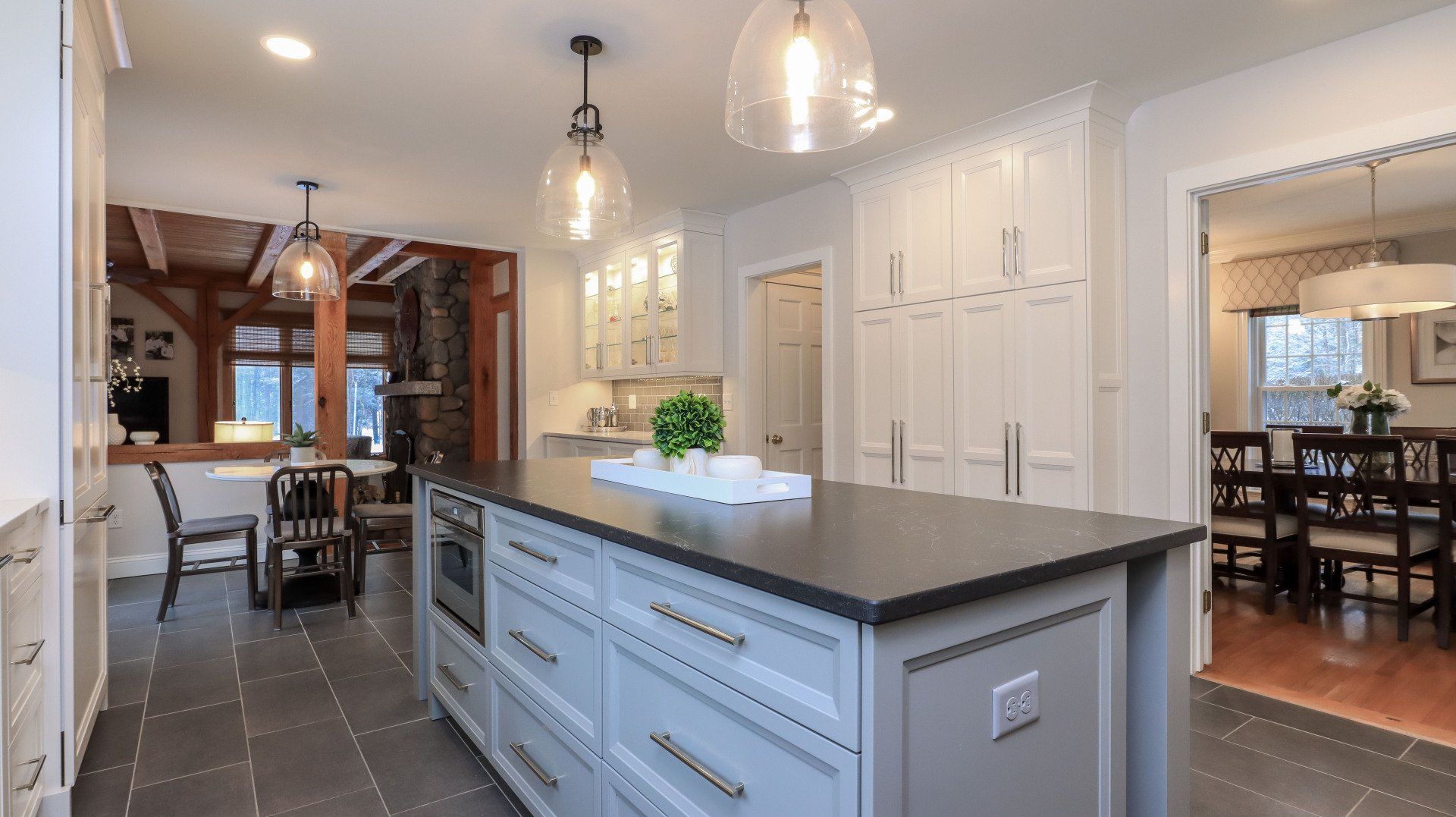Bright kitchen with white cabinets, gray island, pendant lights, and dining area in the background