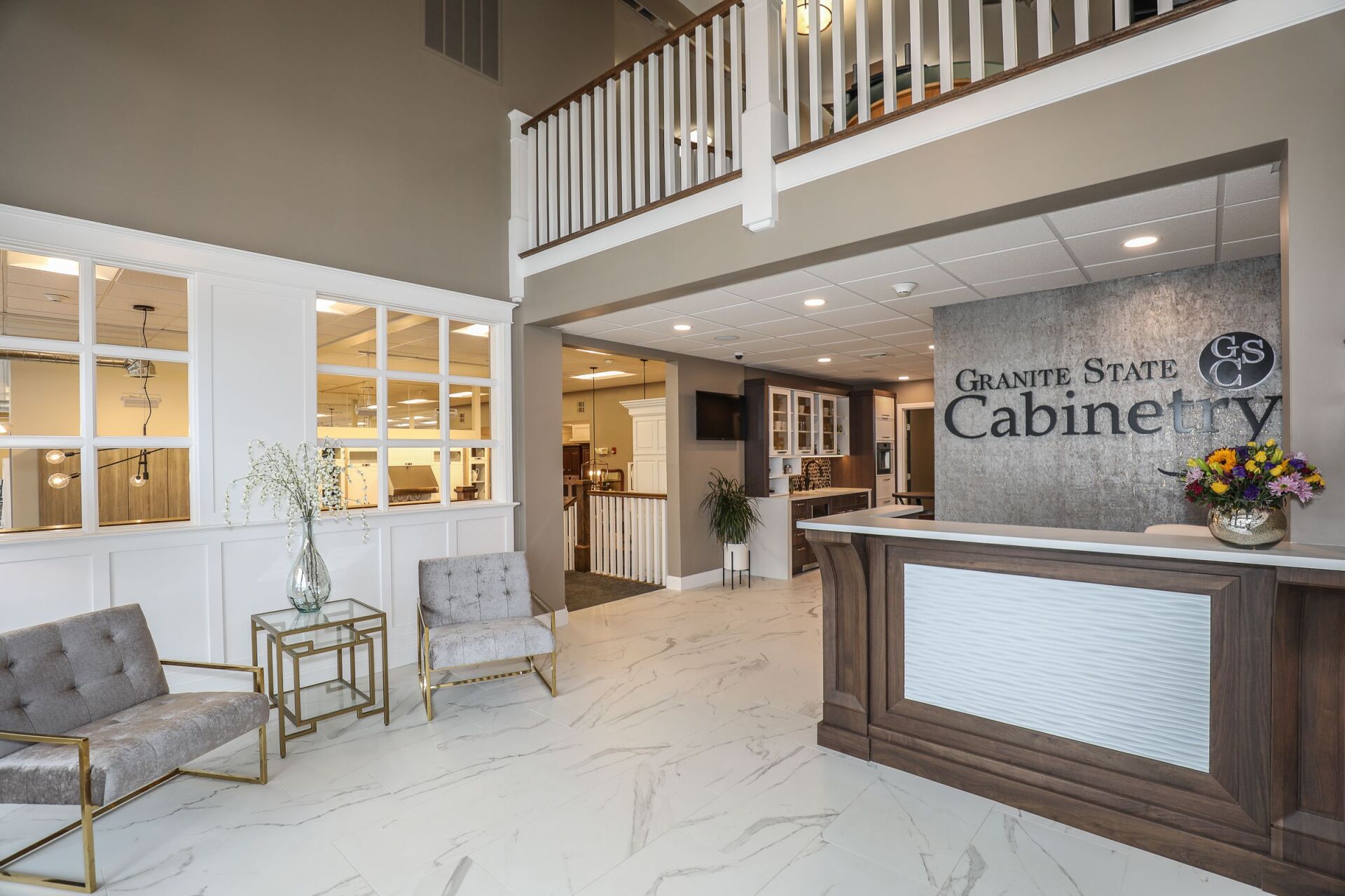 Bright showroom lobby with white marble floors, seating area, reception desk, and “Cabinets” sign