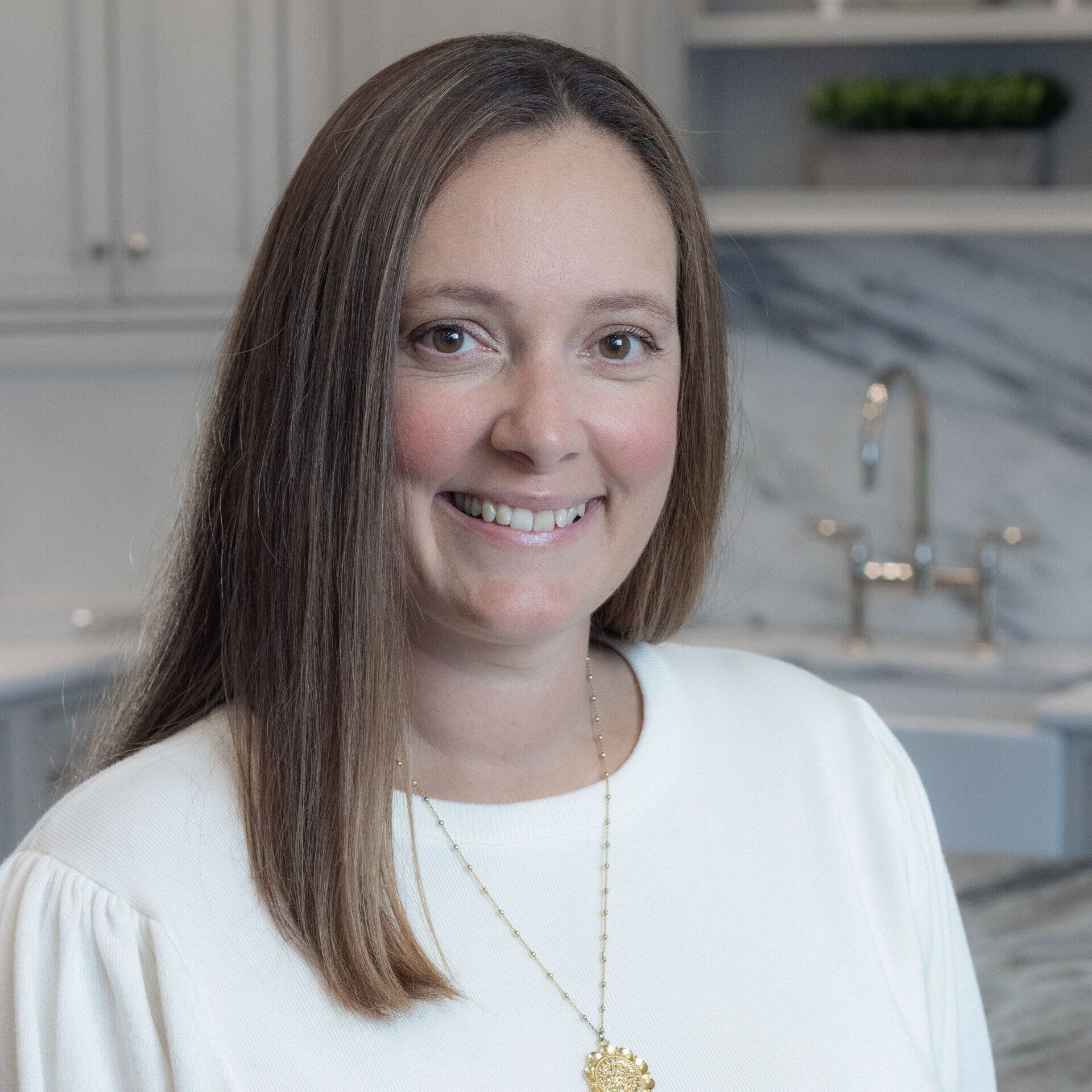 Smiling woman in a white top with long brown hair standing in a bright kitchen