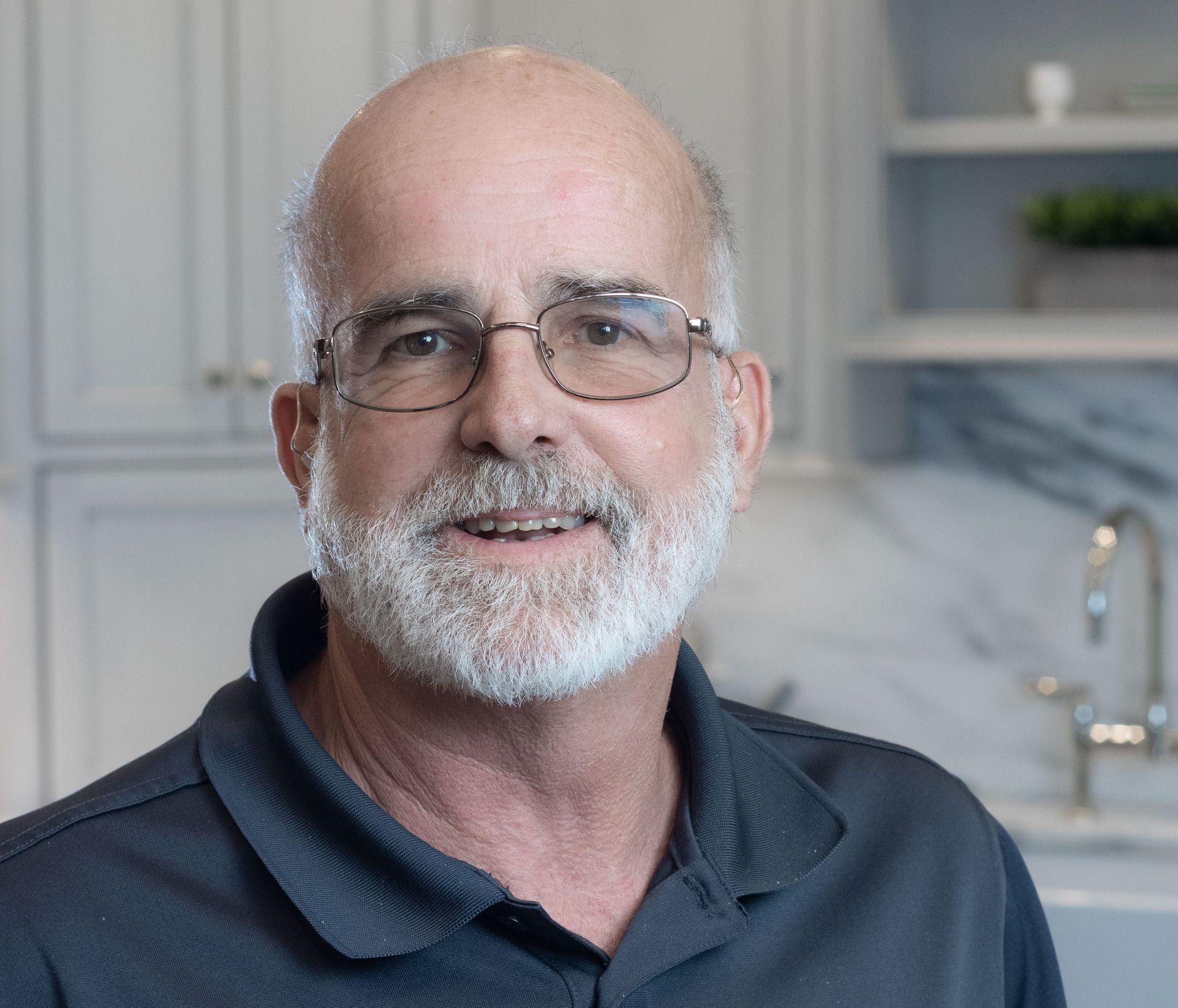 Smiling bald man with glasses in a kitchen, wearing a dark polo shirt.