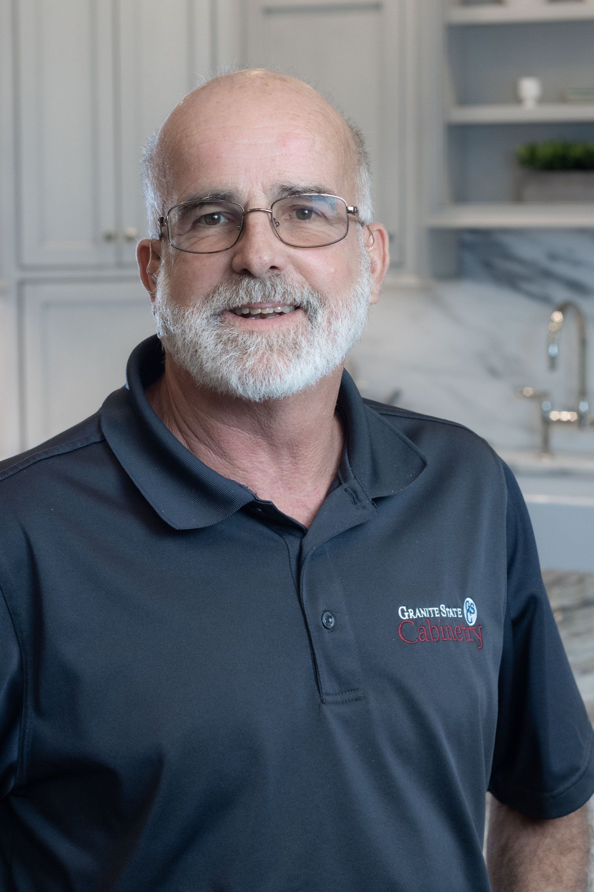 Smiling man in glasses and navy polo shirt standing in a bright kitchen