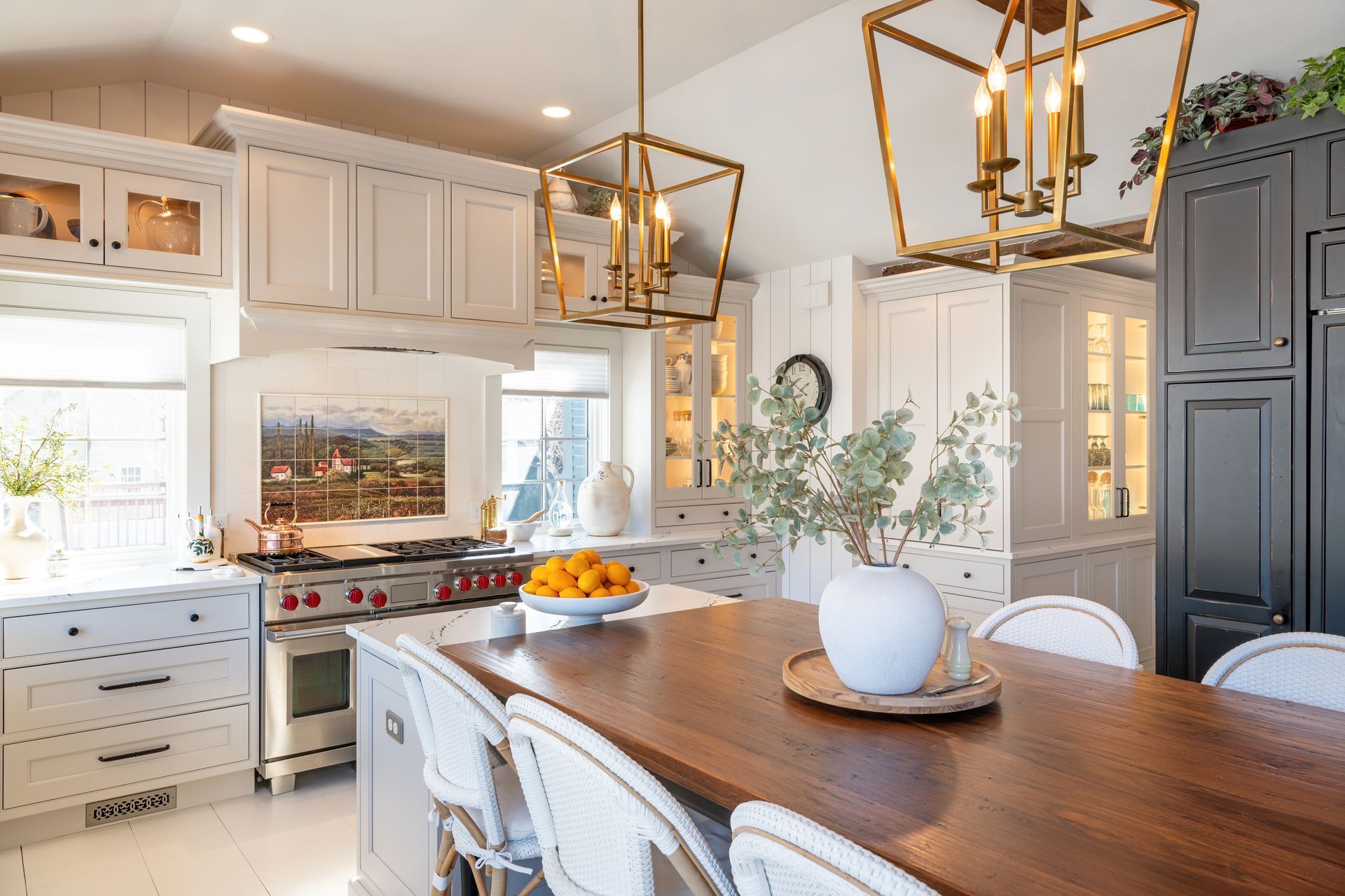 Bright modern kitchen with white cabinets, brass pendant lights, and a wooden dining table