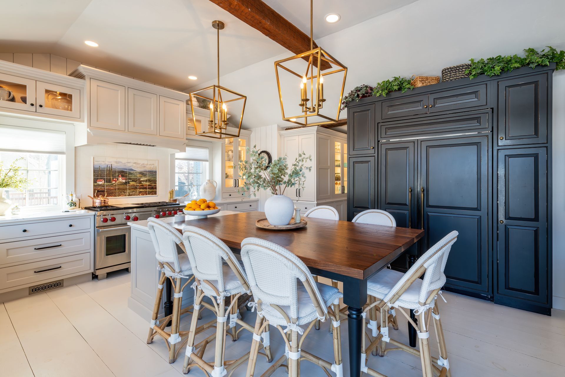 Bright modern kitchen and dining area with white cabinets, wood table, gold pendants, and dark pantry cabinet