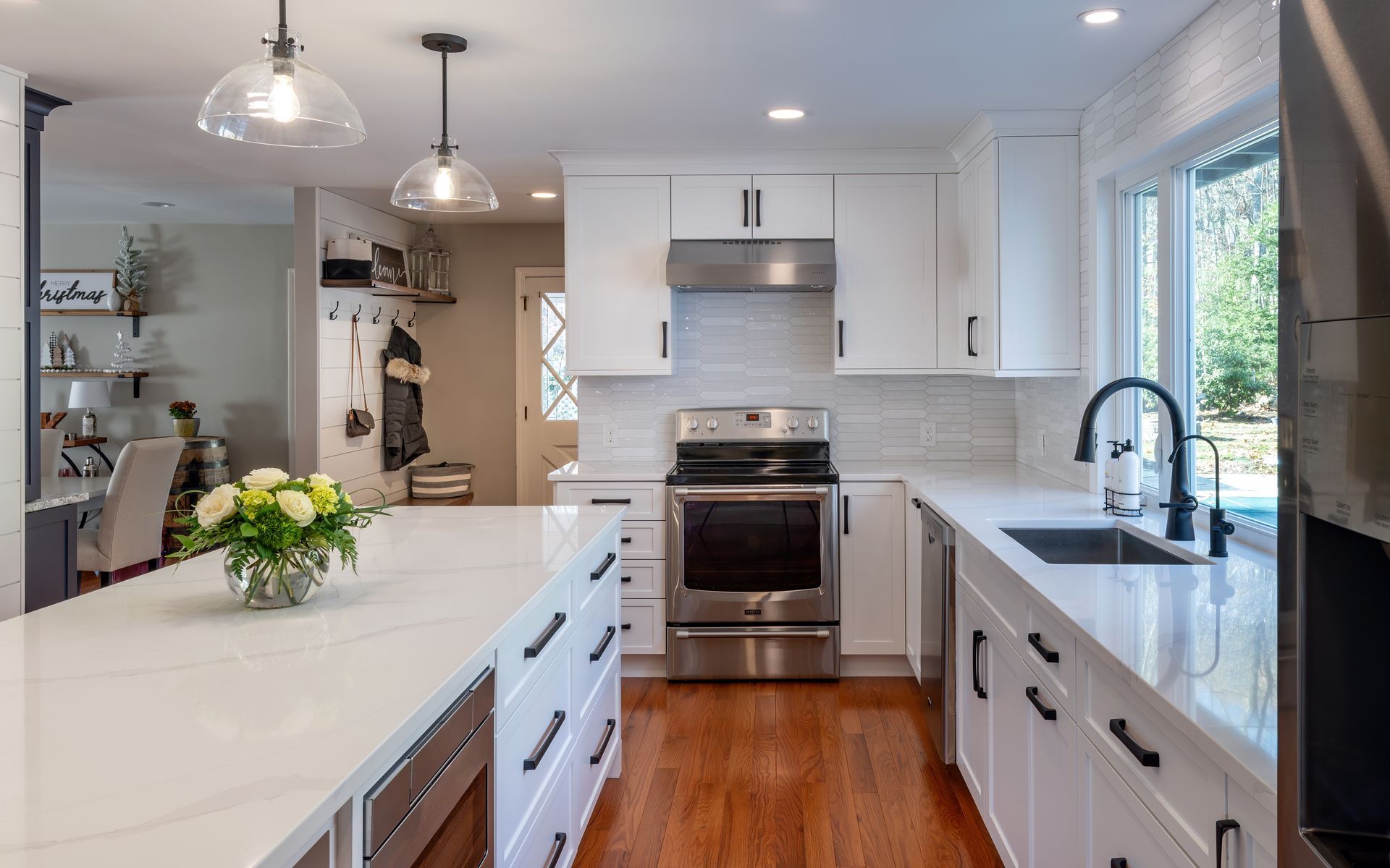 Bright modern kitchen with white cabinets, central island, stainless steel appliances, and large windows