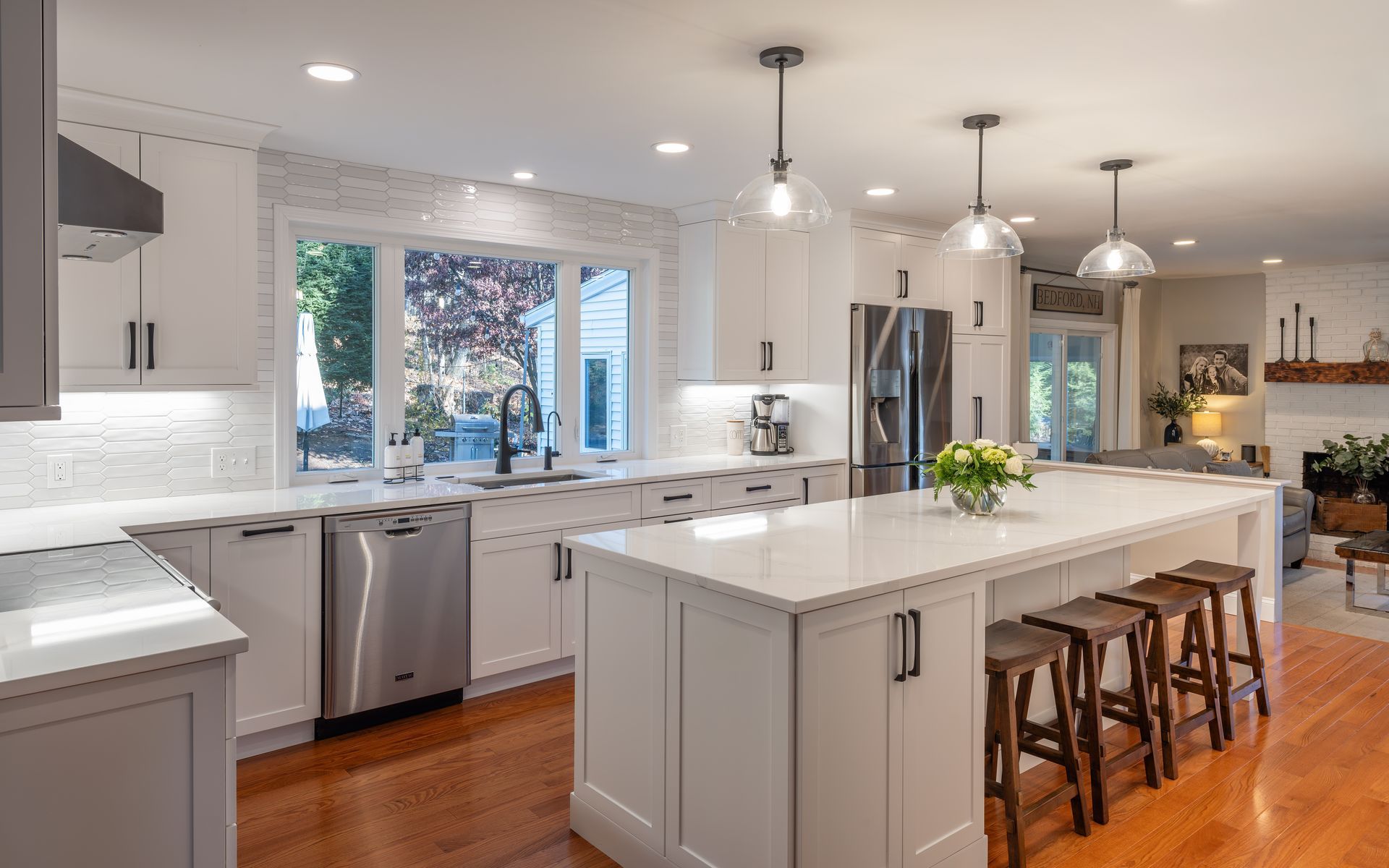 Bright modern kitchen with white cabinets, island, stools, and stainless steel appliances