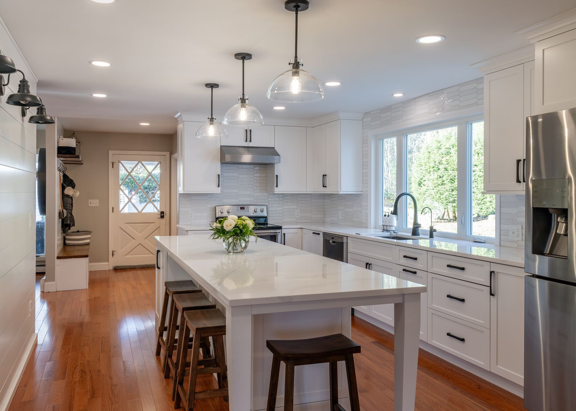 Bright modern kitchen with white cabinets, island, stools, and stainless steel appliances