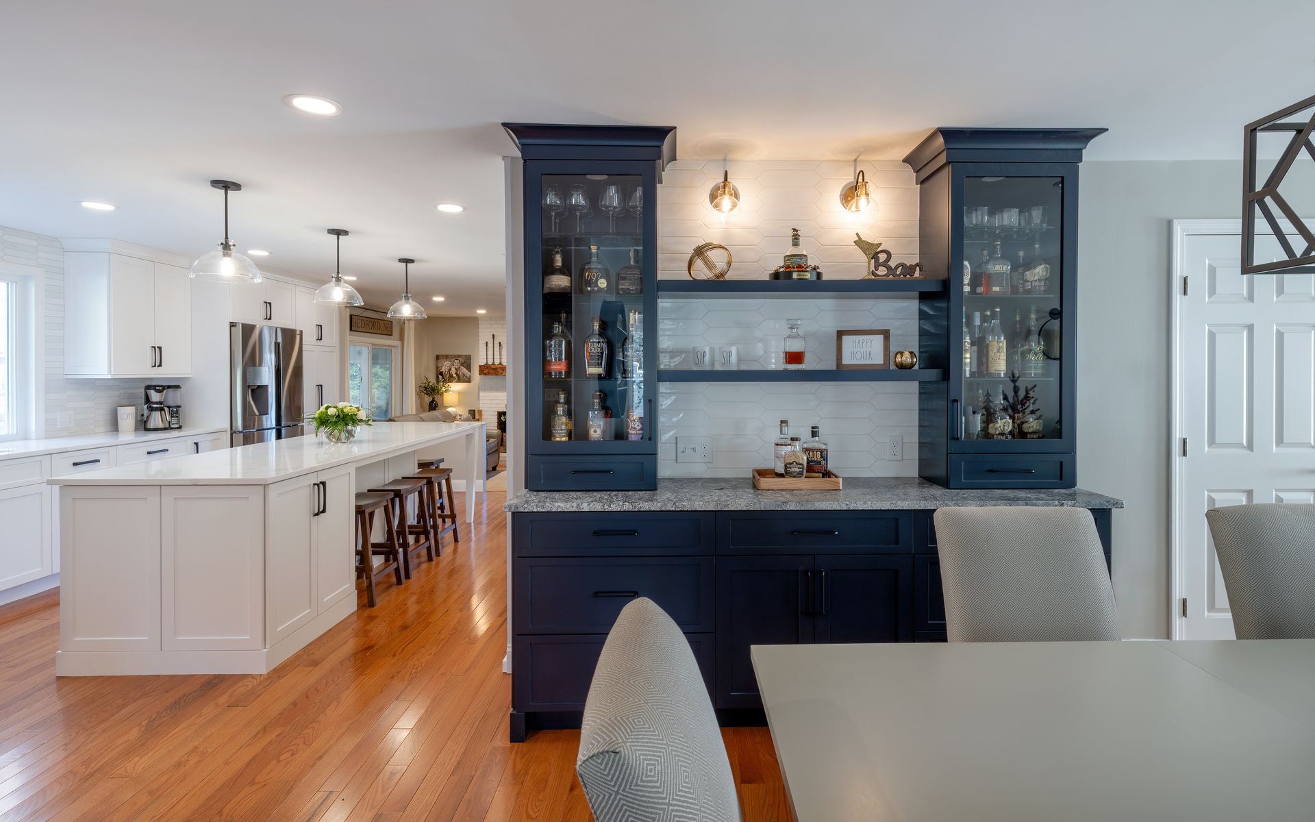 Bright modern kitchen with white island and dark blue cabinetry, warm wood floors, and pendant lights