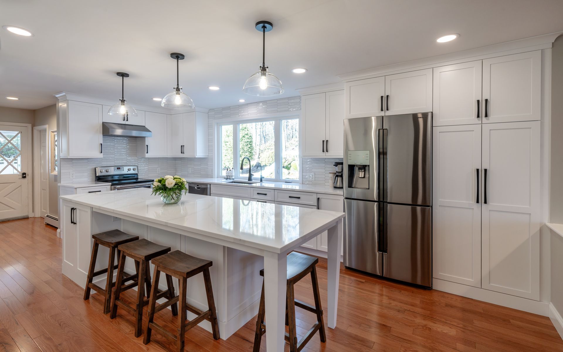 Bright modern kitchen with white cabinets, island, stainless steel appliances, and hardwood floors