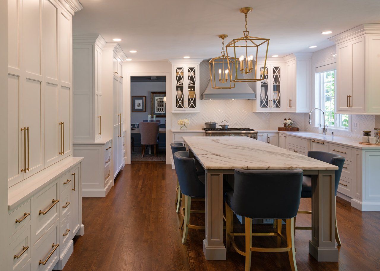 Bright white kitchen with a large marble island, wood floors, and brass pendant lights