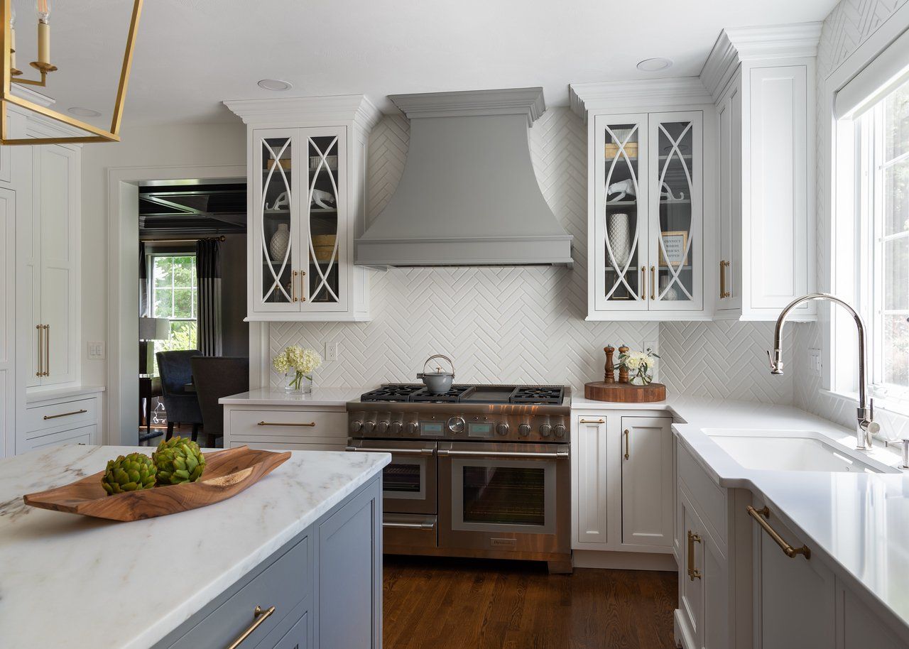 Bright white kitchen with marble island, stainless stove, and large window over the sink