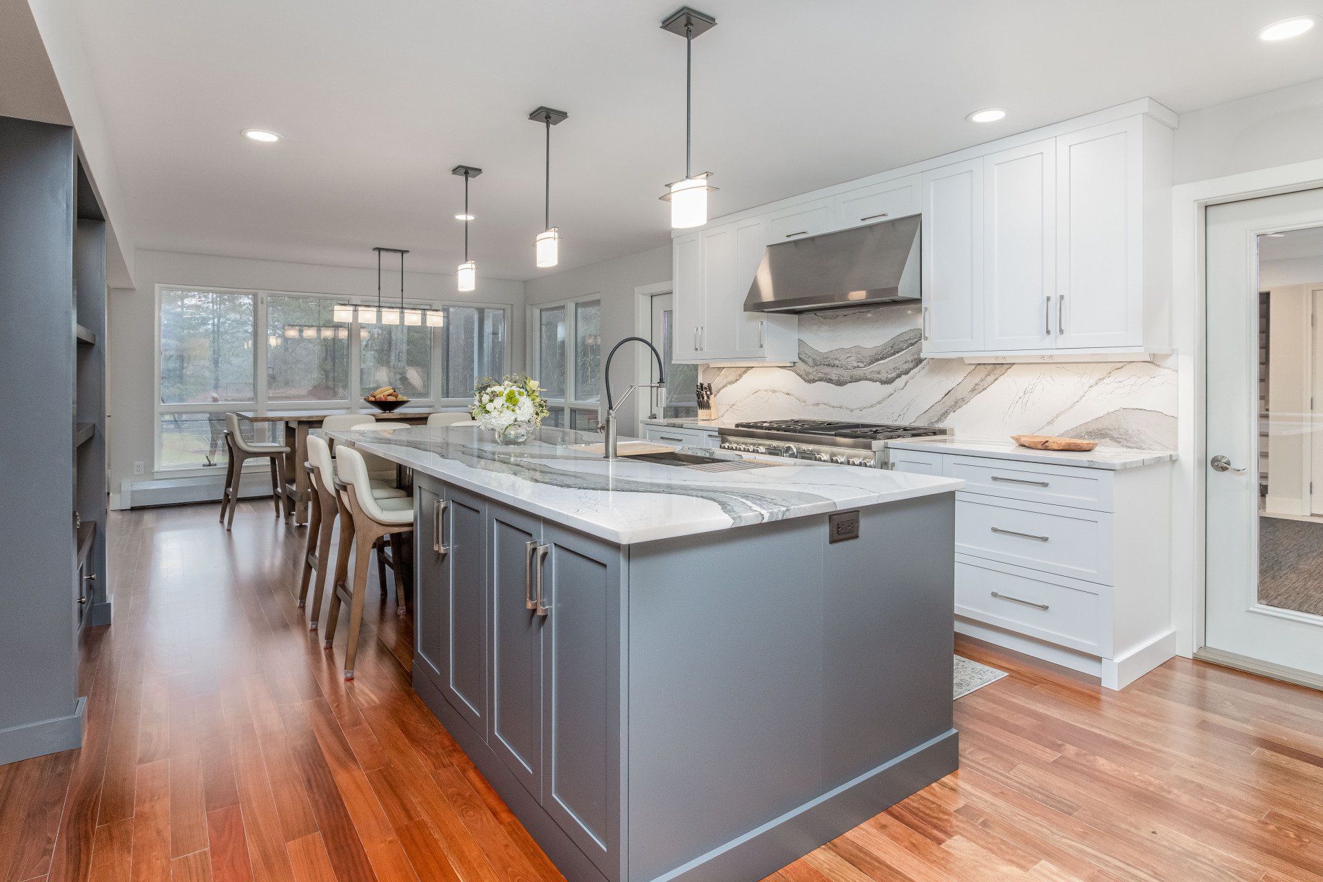 Modern kitchen with gray island, white cabinets, pendant lights, and hardwood floors