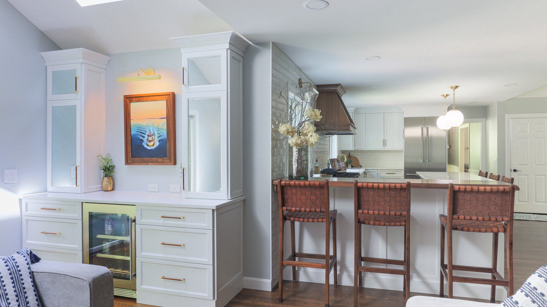 Bright open kitchen and dining area with white cabinets, breakfast bar stools, and framed wall art