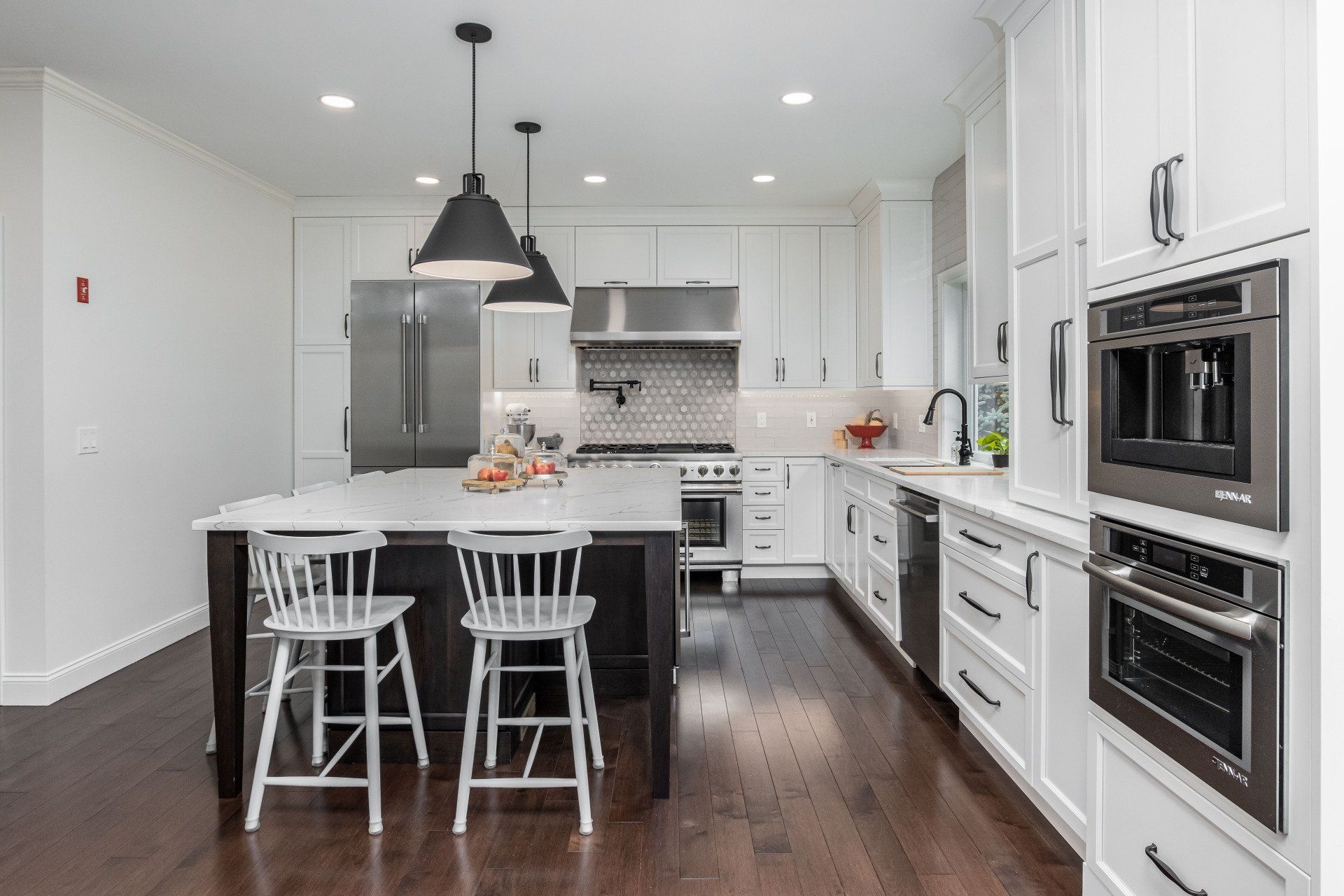 Modern white kitchen with dark island, stainless appliances, and two white stools
