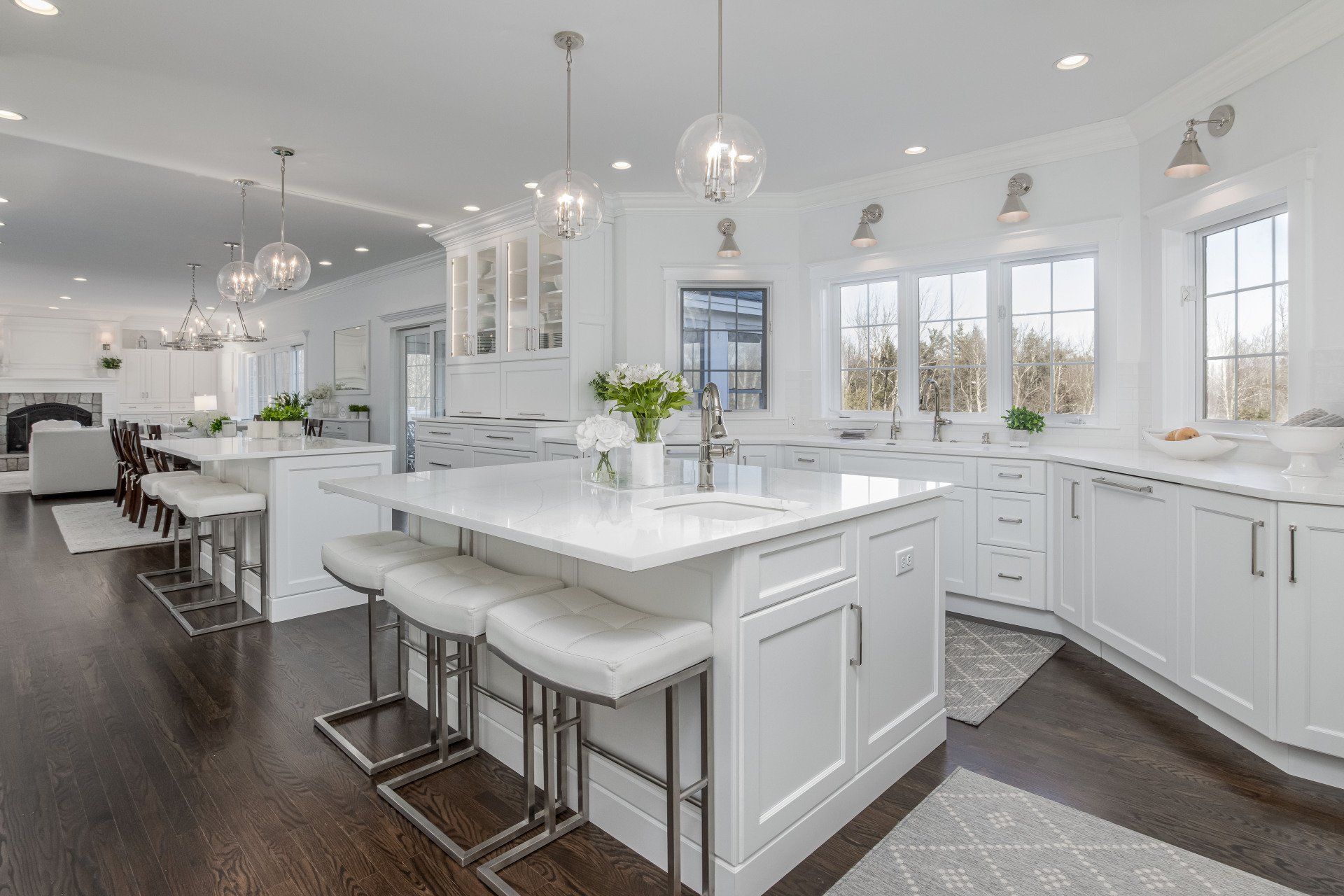 Bright modern white kitchen with island, barstools, pendant lights, and dark hardwood floors