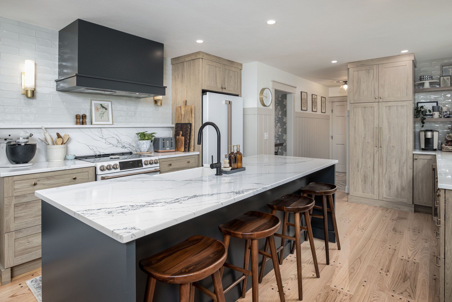 Modern kitchen with a large marble island, dark range hood, and light wood cabinets