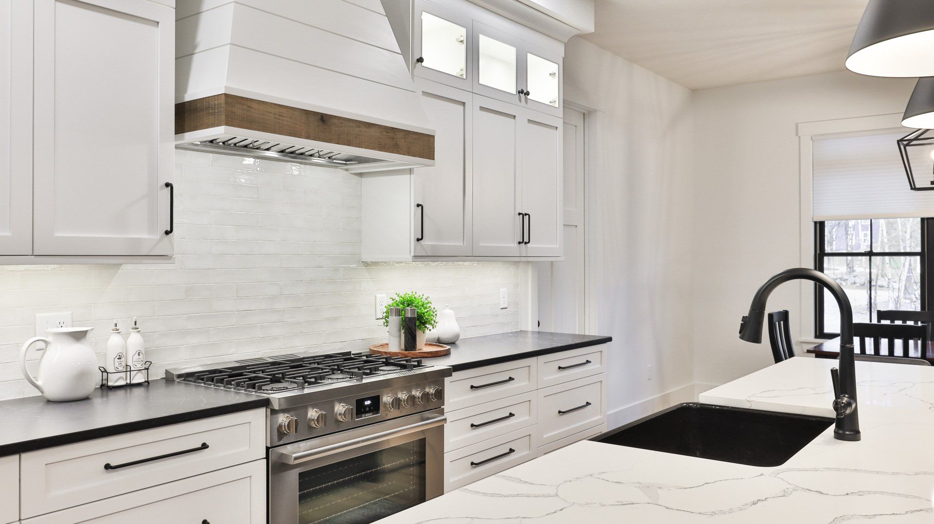 Bright white modern kitchen with marble island, black fixtures, and large windows