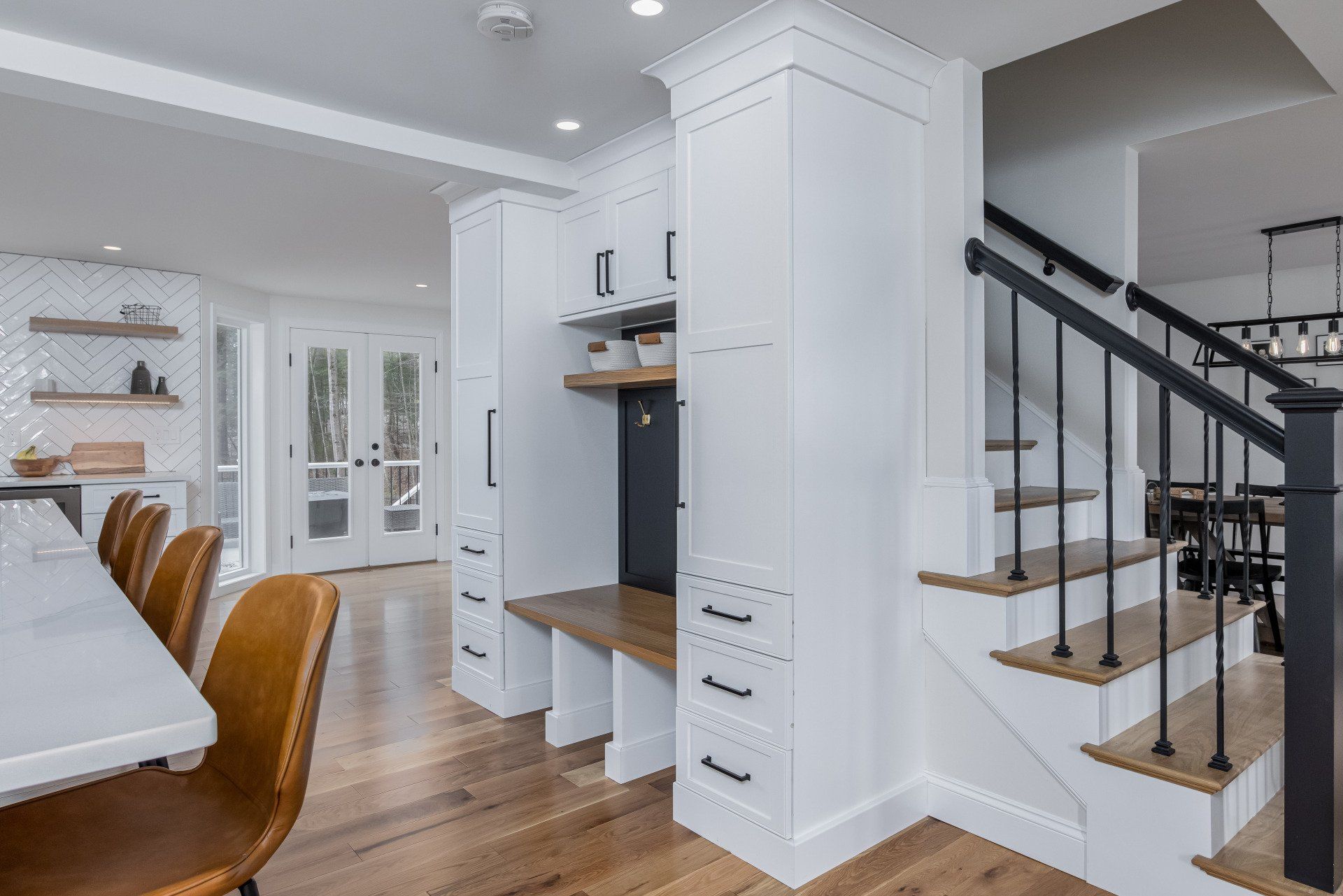 Bright dining room with white cabinets, wooden chairs, and a staircase with black railing.