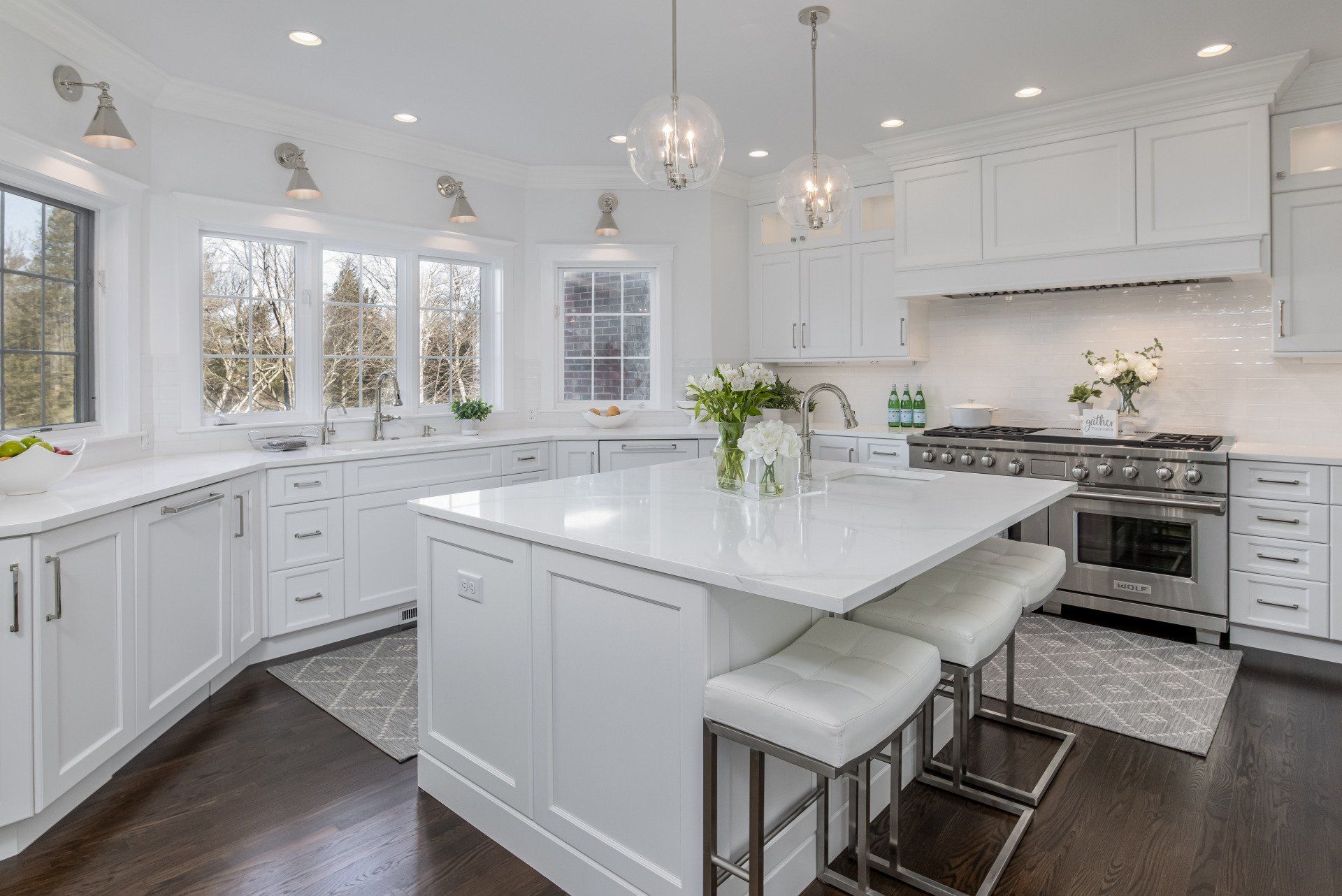 Bright white modern kitchen with island, stainless steel appliances, and large windows