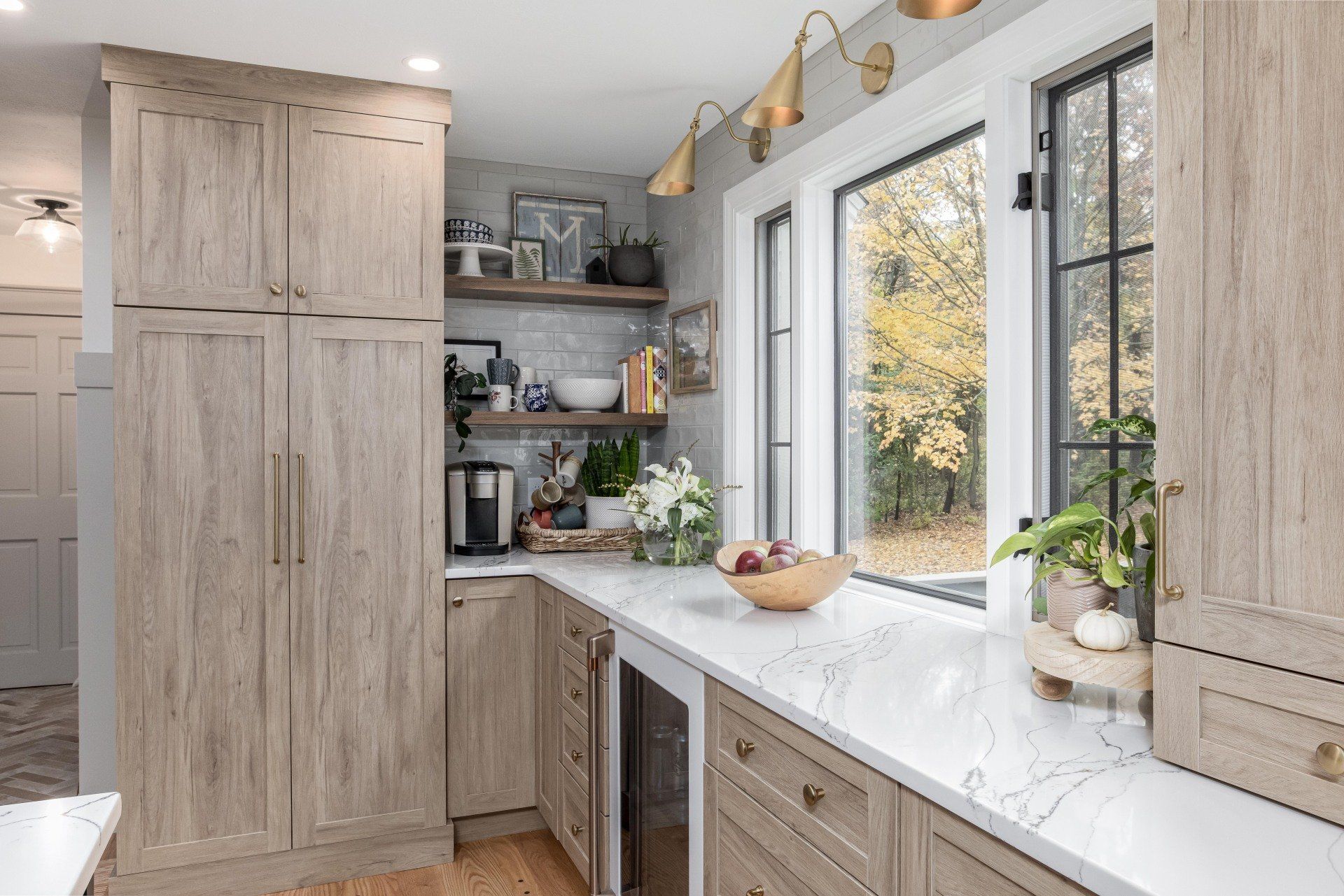 Bright kitchen with light wood cabinets, white countertop, large window, and potted plants.