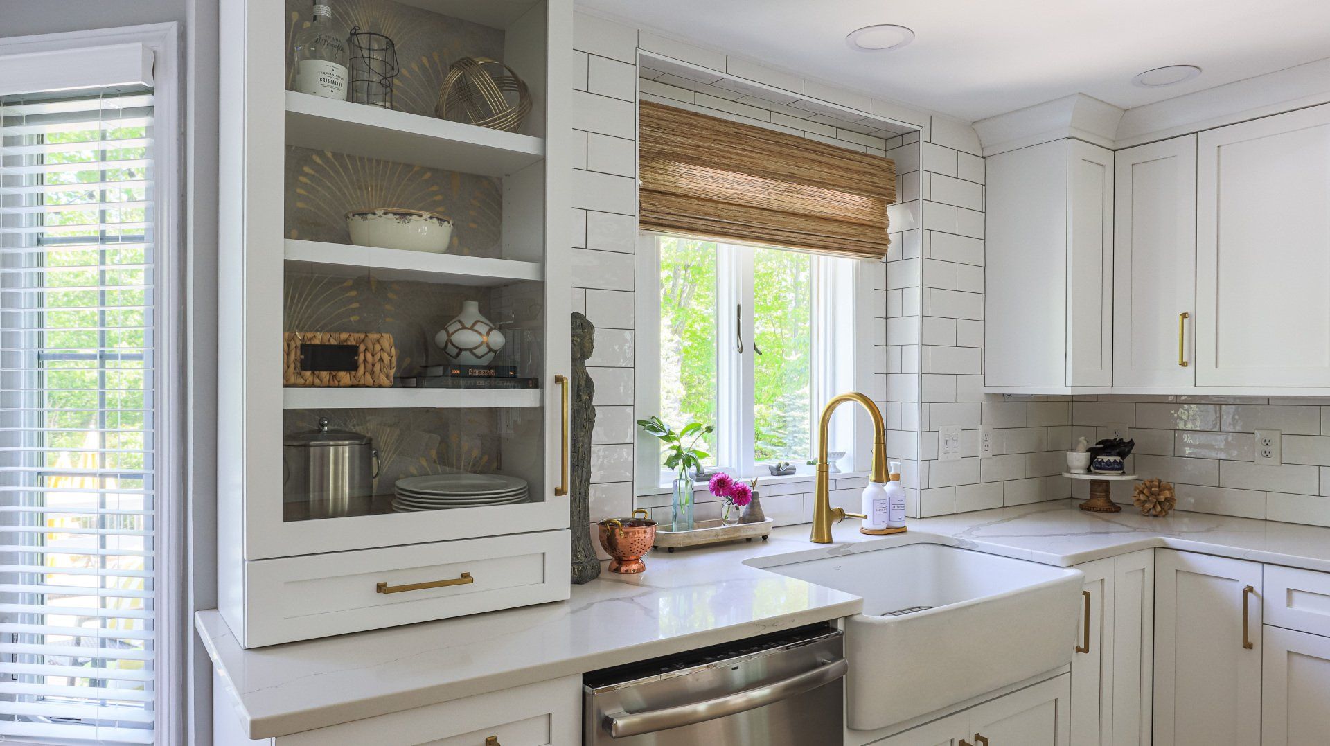 Bright white kitchen with open shelves, farmhouse sink, brass faucet, and window with woven shade