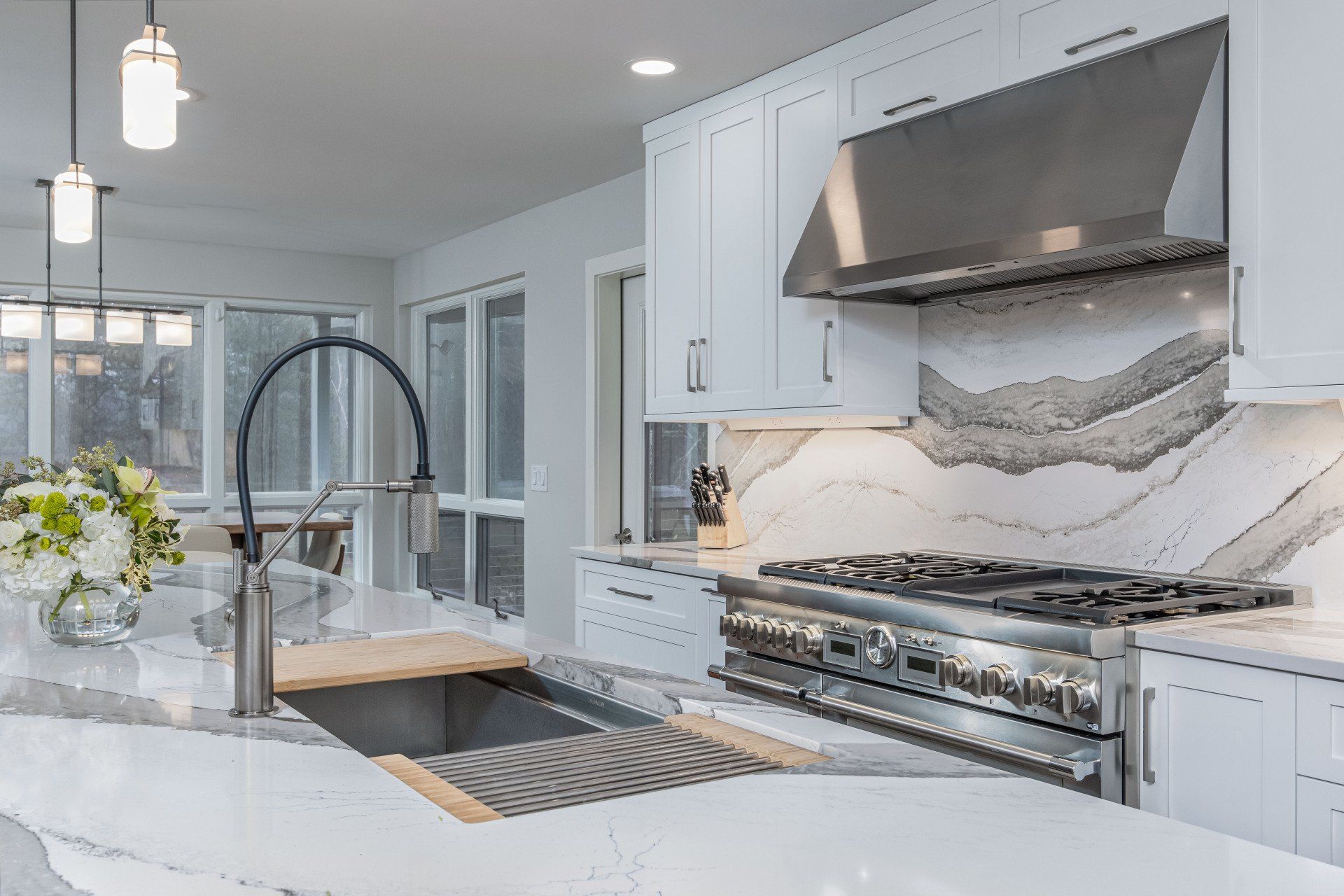 Modern white kitchen with marble island, black faucet, stainless range, and large windowed dining area
