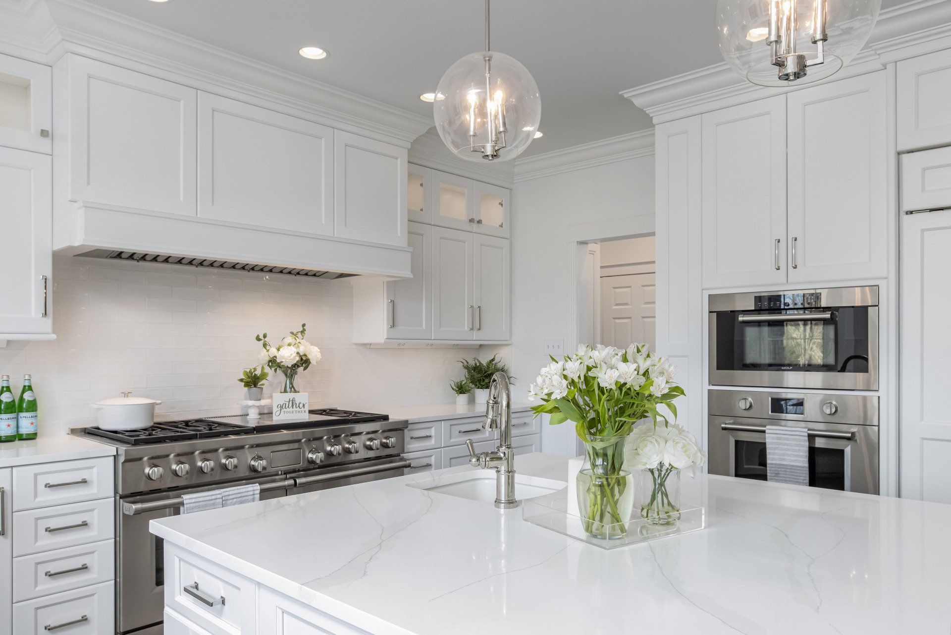 Bright white modern kitchen with island, stainless steel appliances, and flowers on the counter