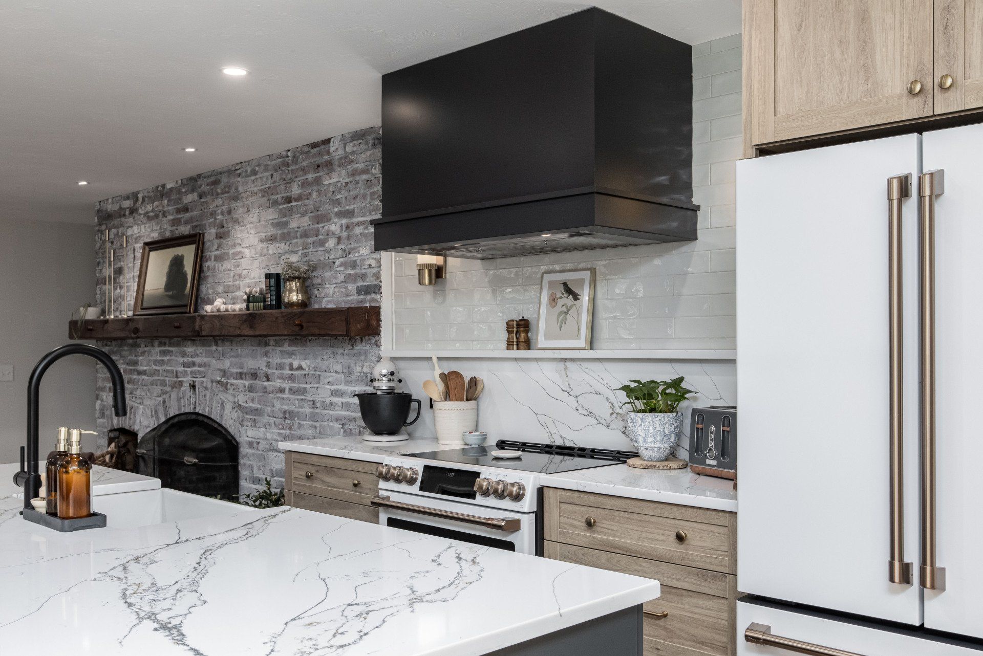 Modern kitchen with marble island, white cabinets, black range hood, and gray brick backsplash