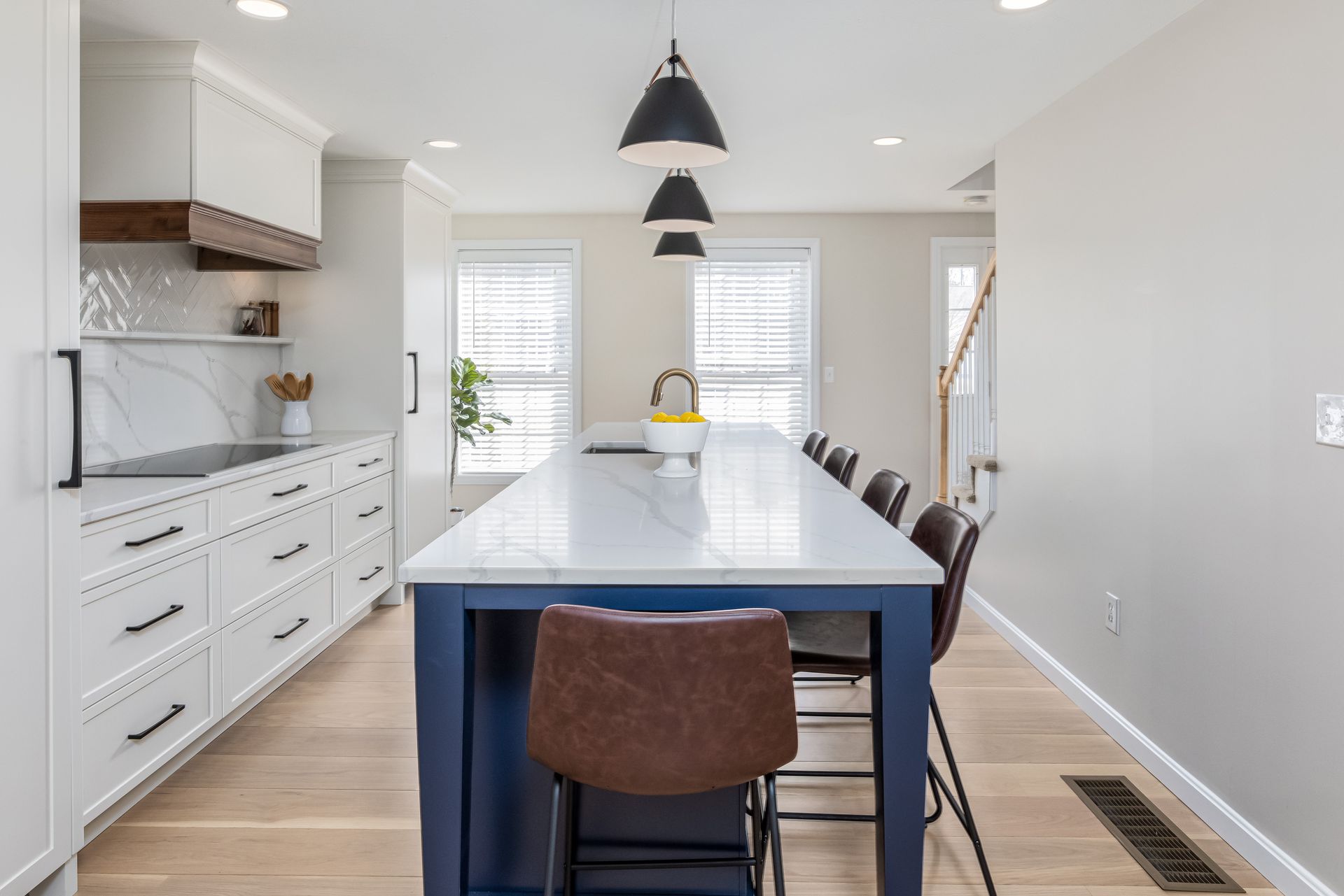 Bright modern kitchen with a navy island, white cabinets, pendant lights, and wood floors