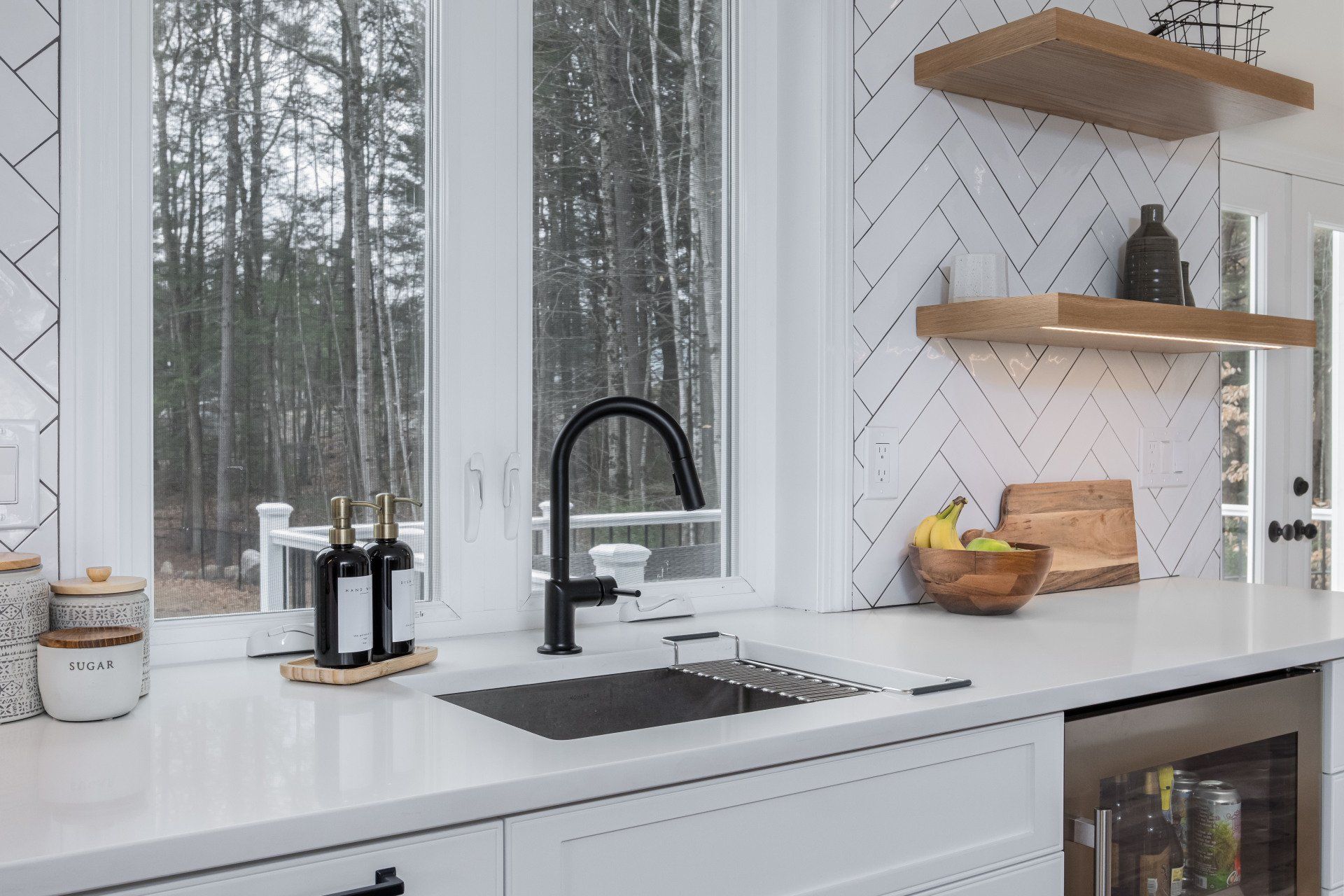 Modern white kitchen with black faucet, sink, open shelves, and forest view through large windows