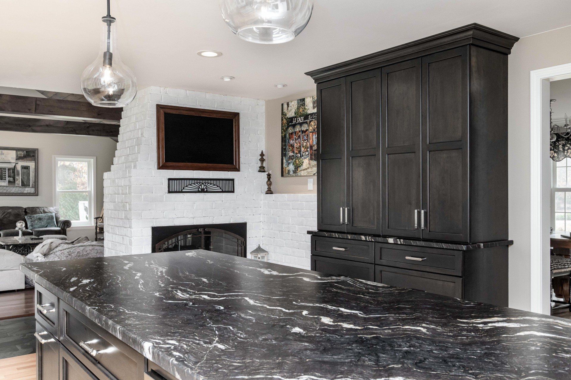 Modern kitchen with dark cabinetry, black marble island, pendant lights, and a white fireplace wall