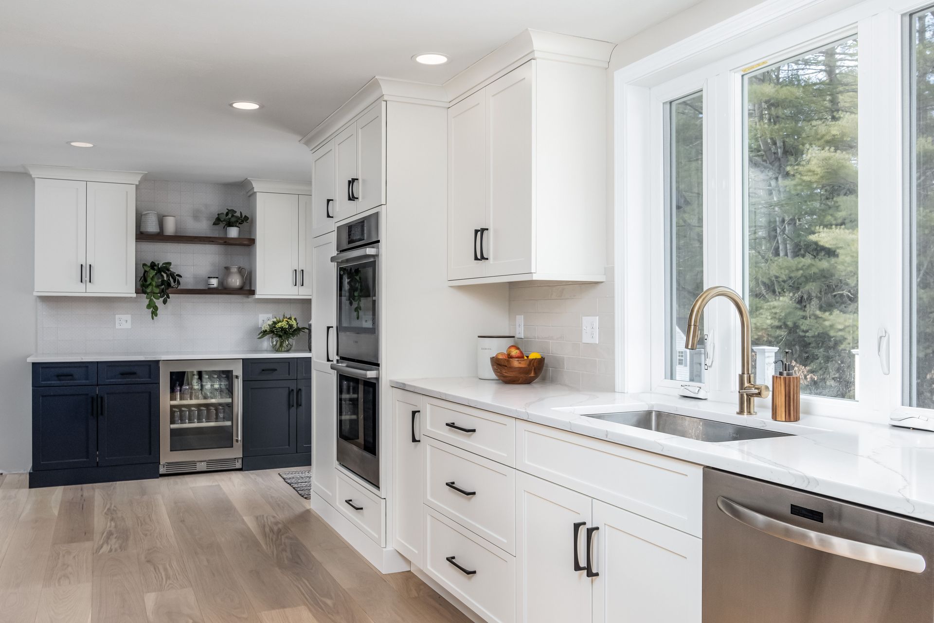 Bright modern kitchen with white cabinets, light wood floors, and large windows over a sink