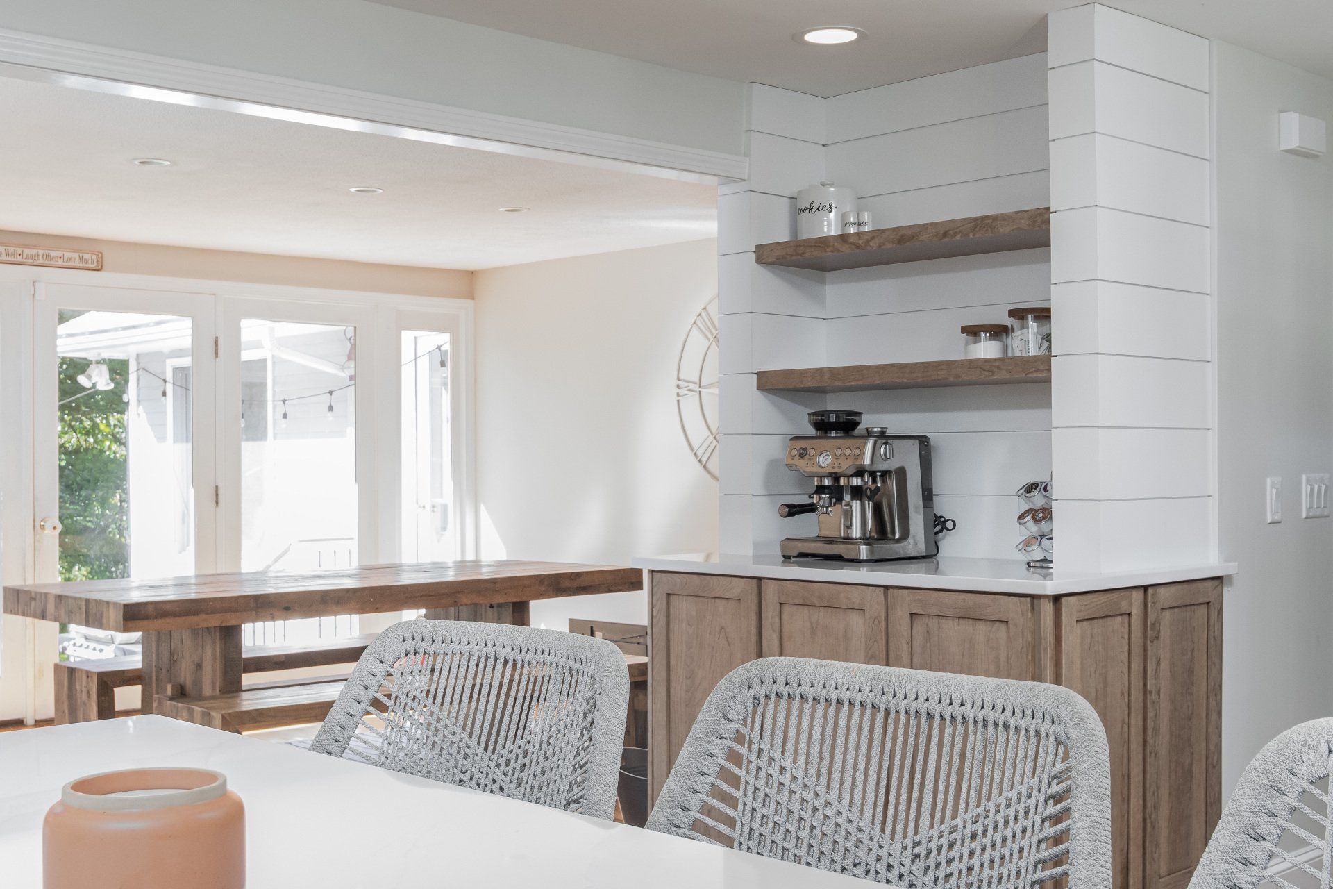 Bright modern kitchen and dining area with white cabinetry, wood accents, and woven chairs