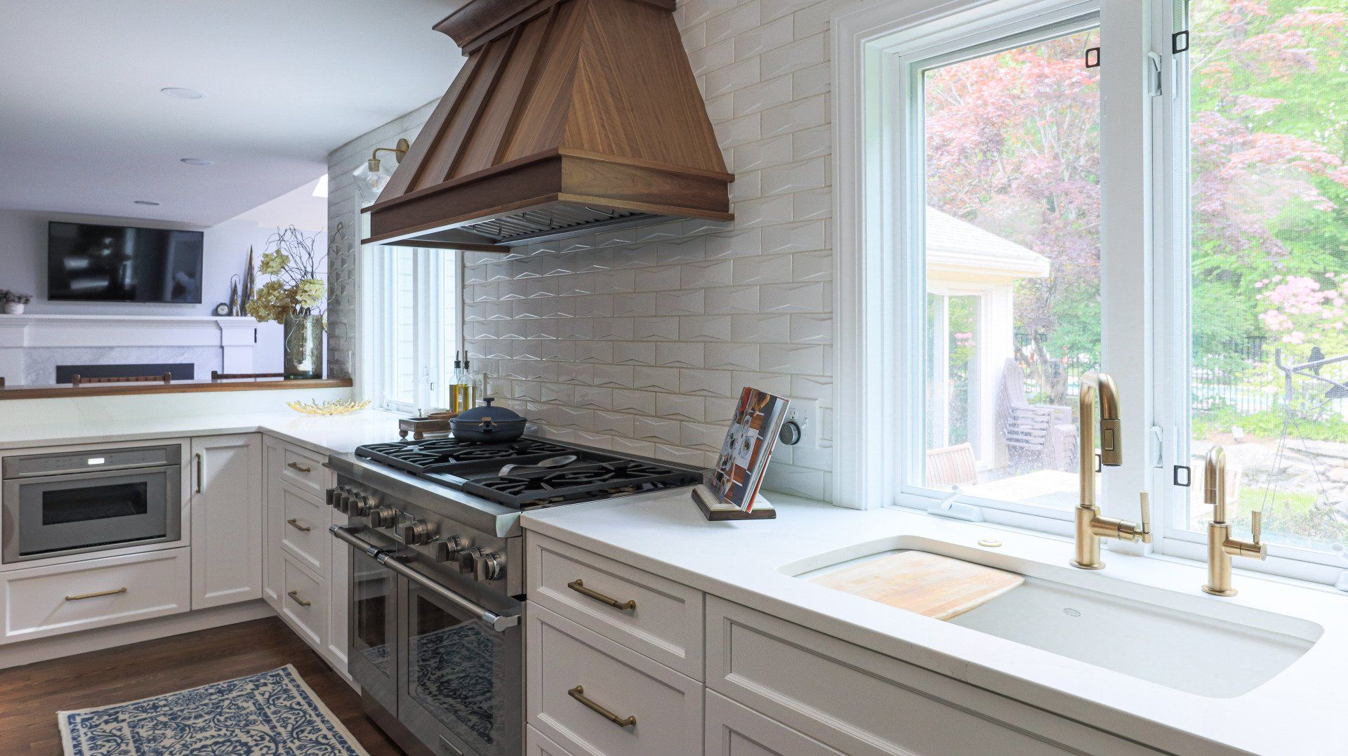 Bright kitchen with white cabinets, gas stove, copper hood, and a sunlit sink by a window