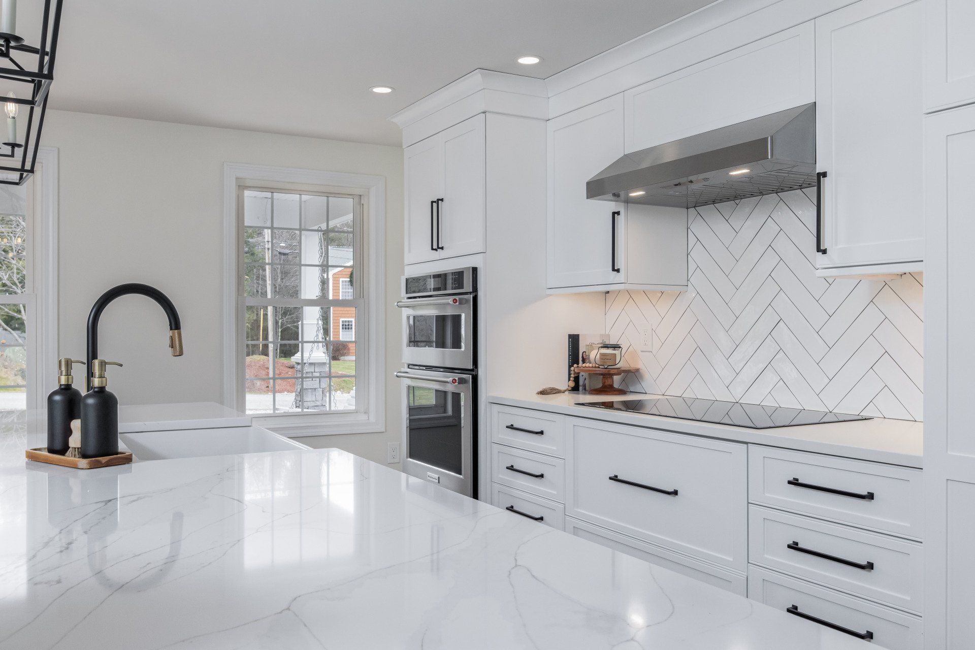 Bright white modern kitchen with marble island, built-in oven, and herringbone tile backsplash