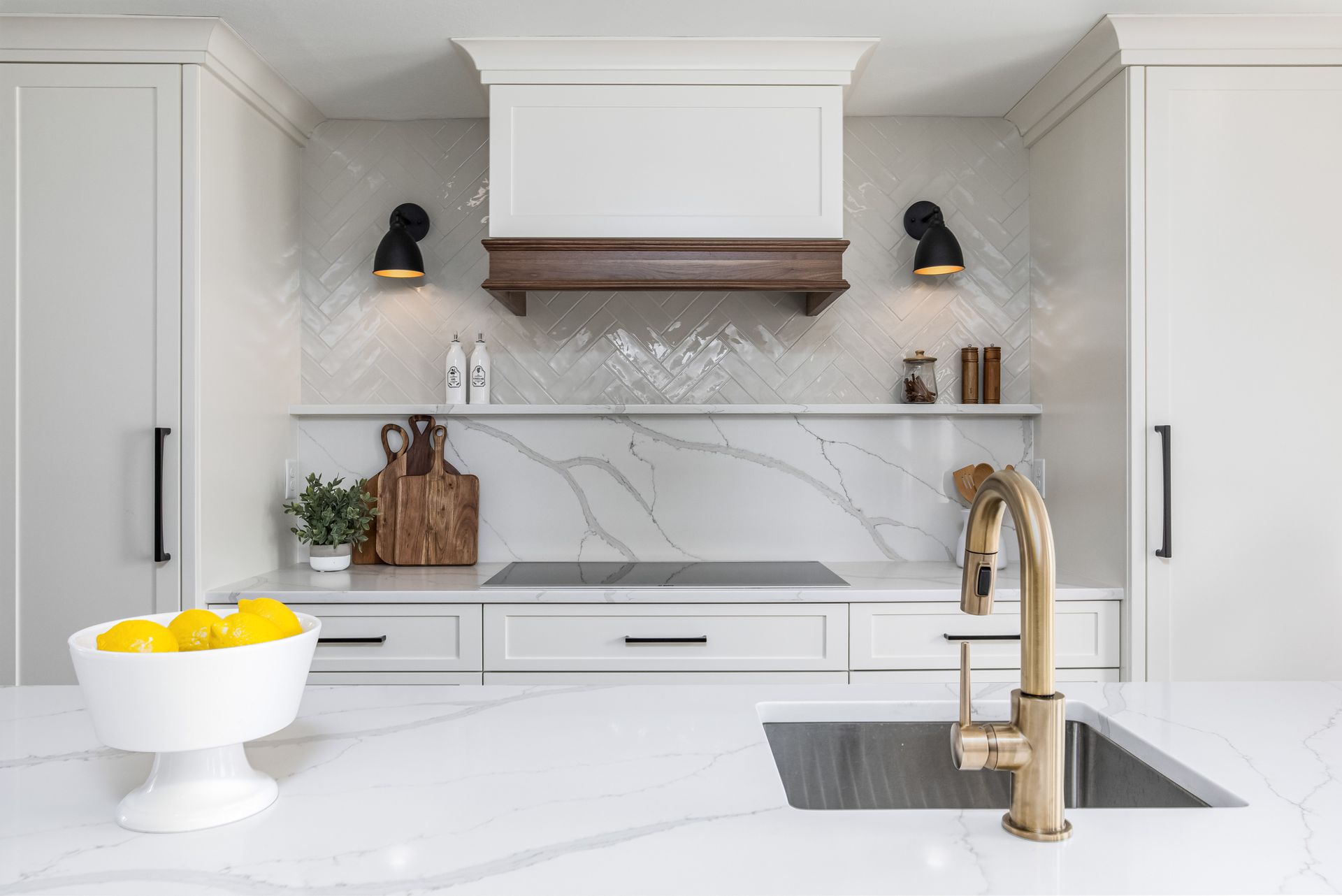 Bright white kitchen with marble island, brass faucet, open shelves, and wood range hood