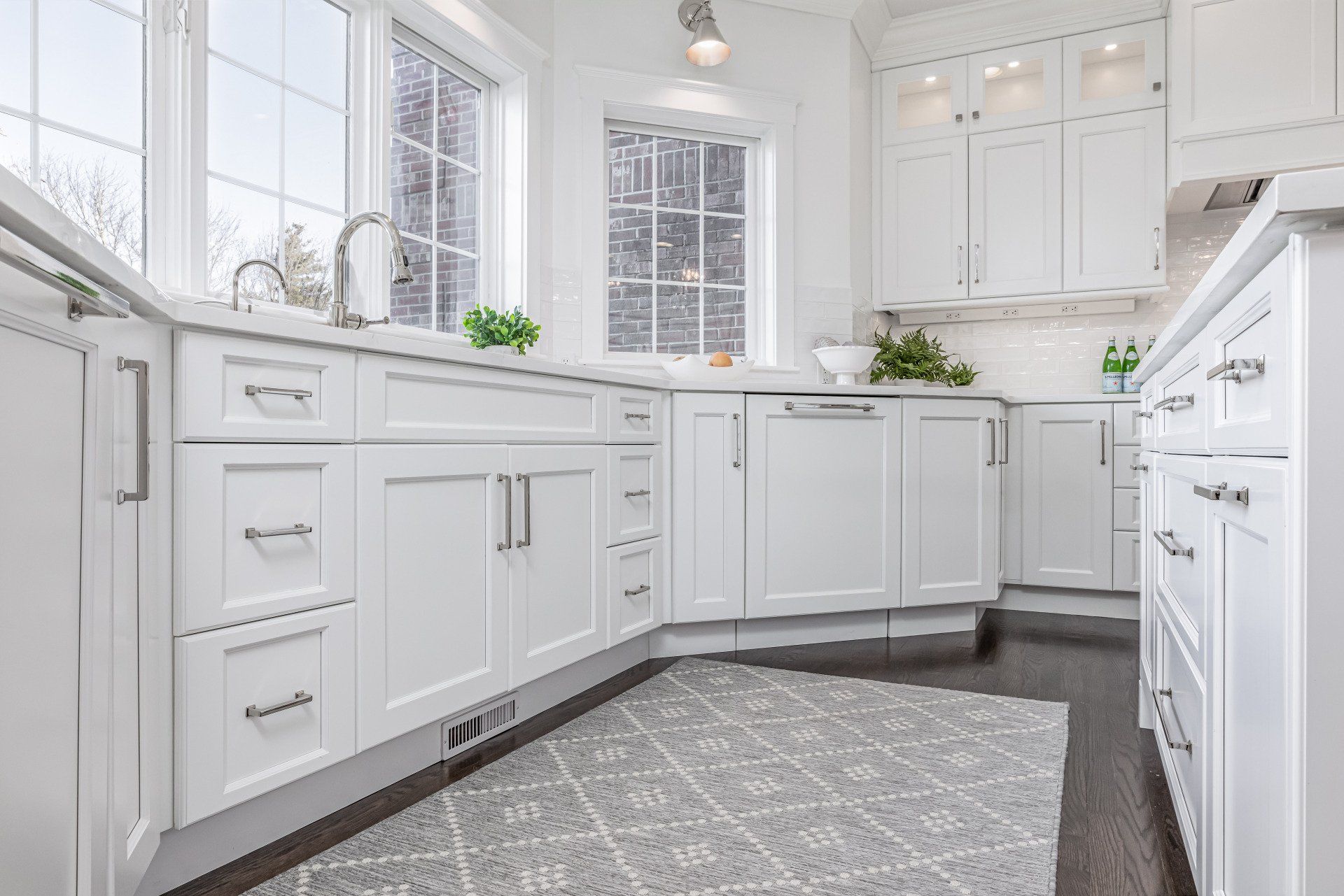 Bright white modern kitchen with cabinets, window, and patterned gray rug
