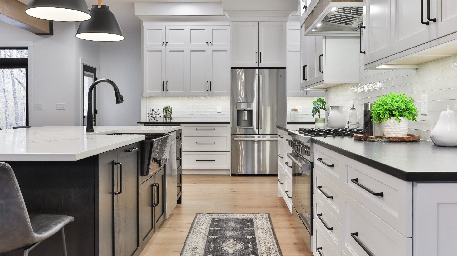 Bright modern kitchen with white cabinets, stainless steel appliances, black countertops, and a wooden floor.