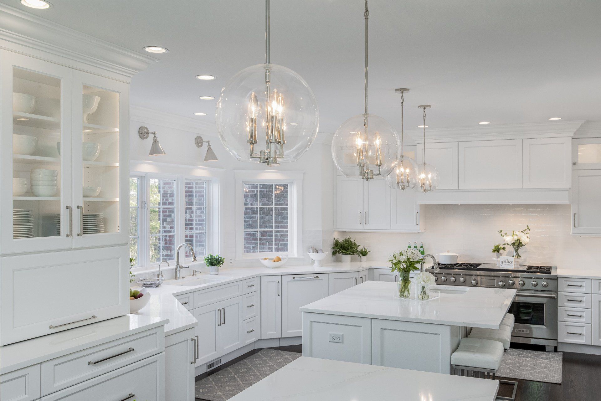 Bright white modern kitchen with marble island, glass cabinets, and hanging pendant lights