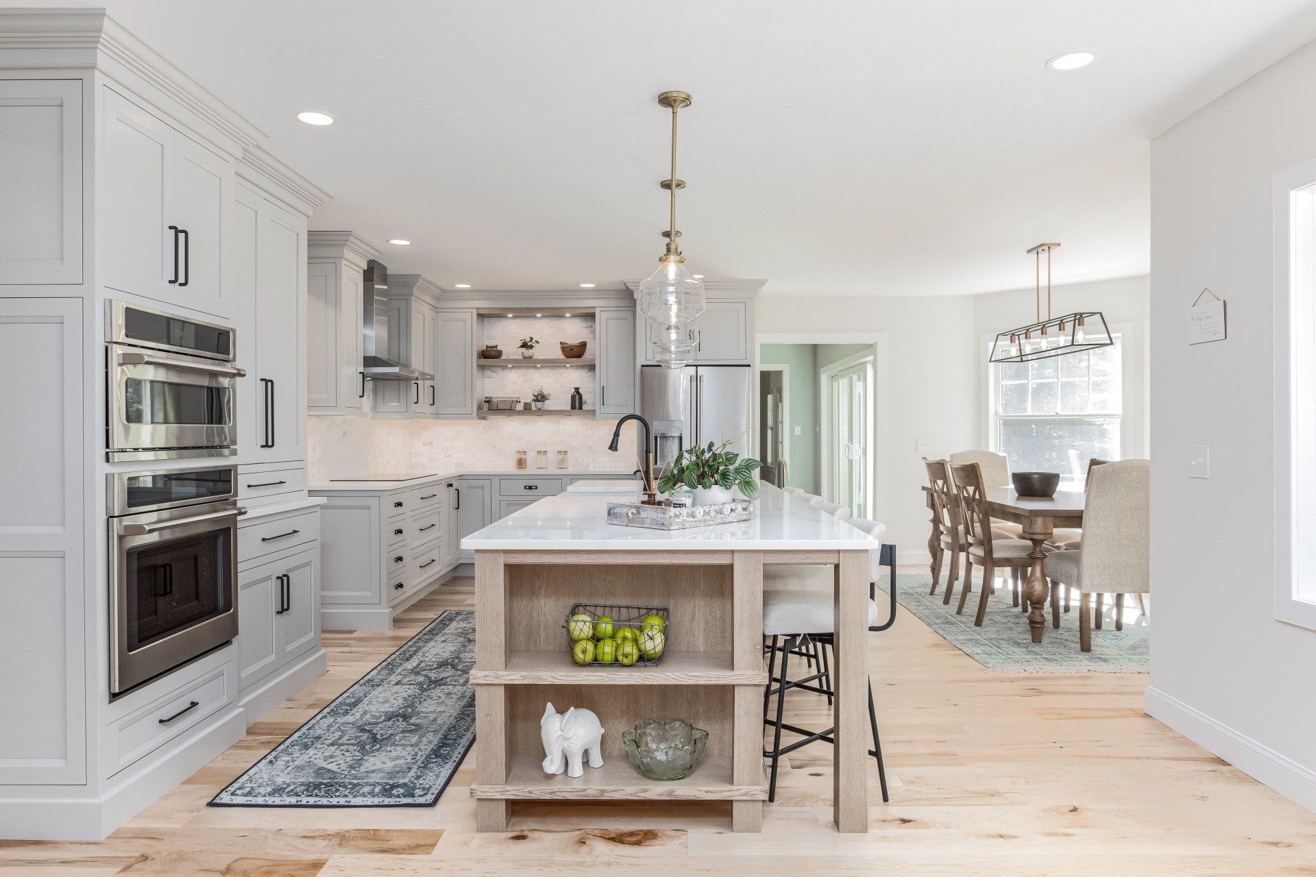 Bright white kitchen with island, built-in ovens, and adjoining dining area with wood floors