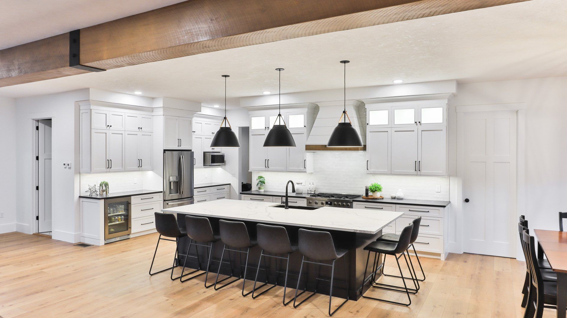 Bright modern kitchen with a large island, black chairs, white cabinets, and hanging pendant lights